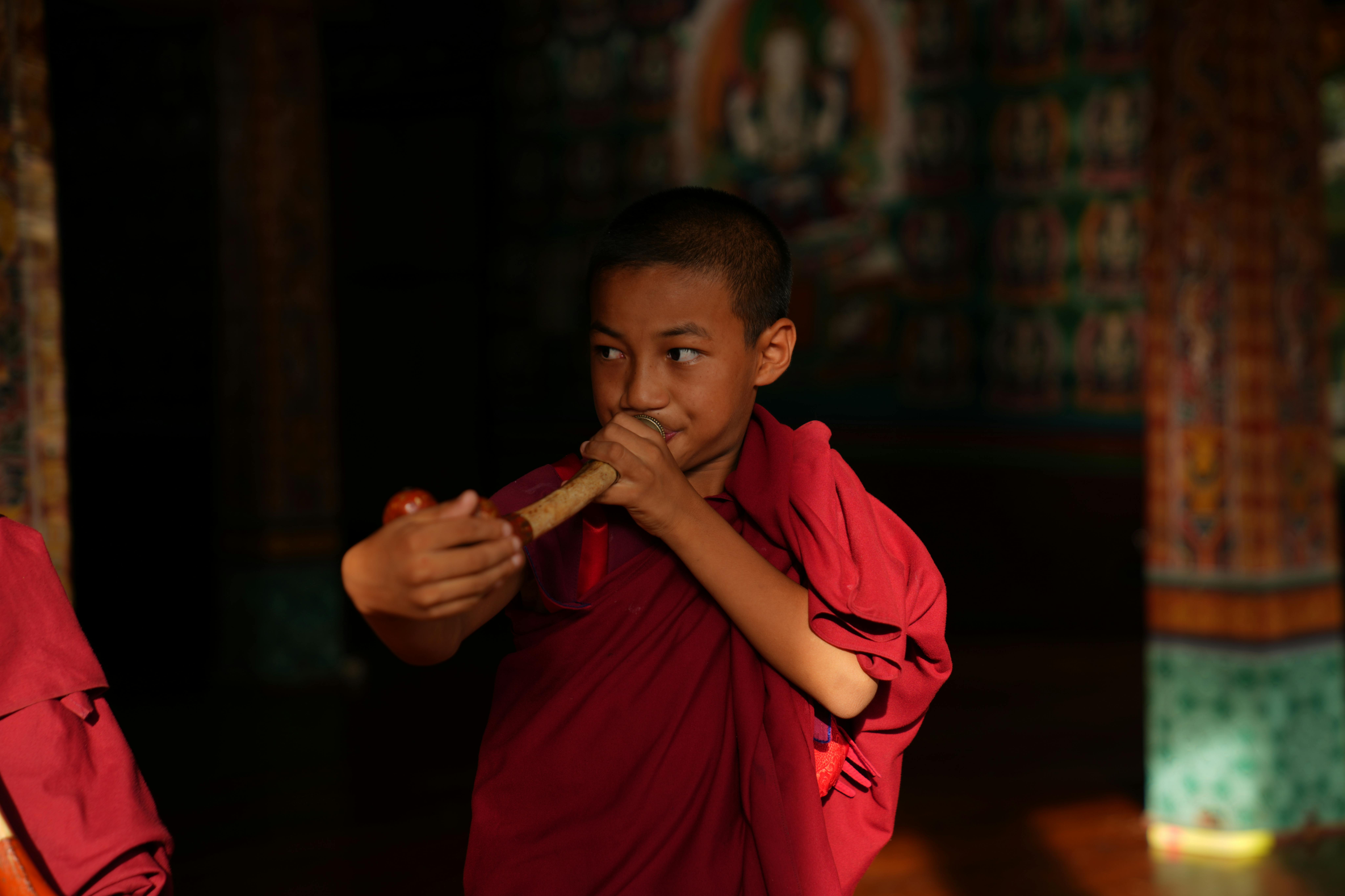Un giovane monaco utilizza uno strumento musicale cerimoniale in osso, impiegato nei rituali. Siamo in Bhutan, nella scuola monastica Phochu Dumra