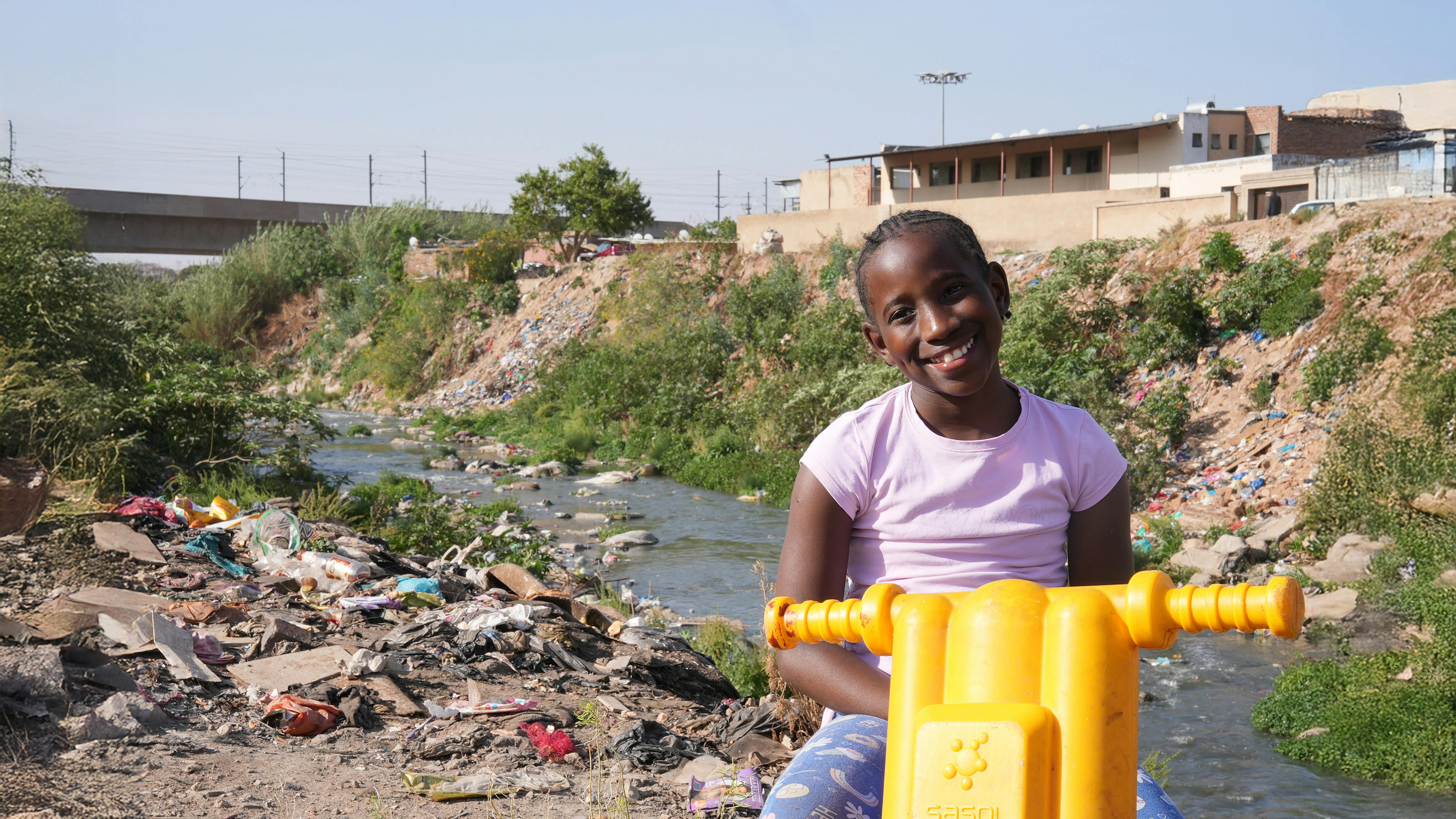 Sudafrica, Ompfuna Nkhumeleni, una ragazza di 10 anni, posa per un ritratto, seduta sulla sua moto di plastica accanto al fiume inquinato Juskei.