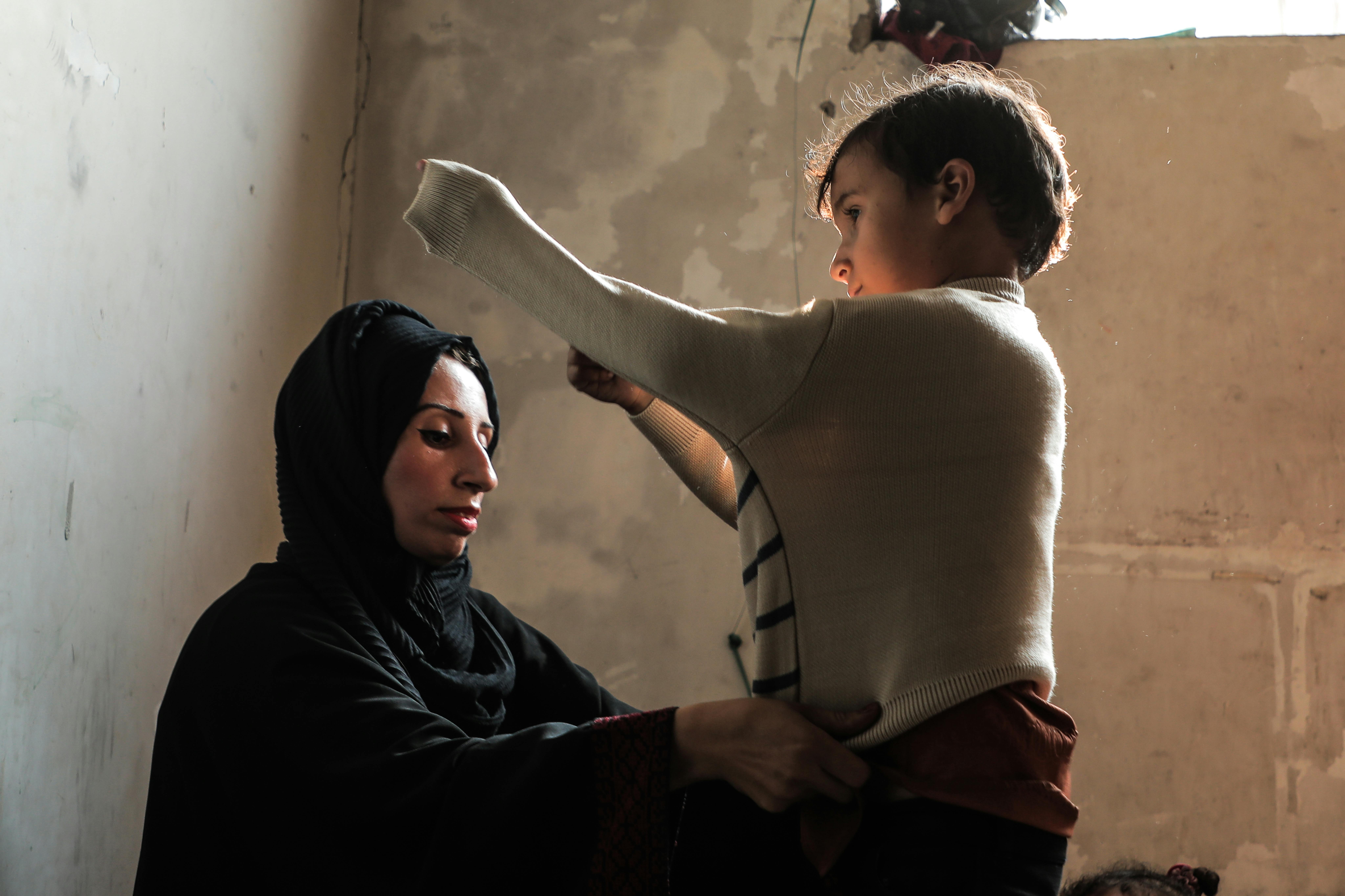 Arriva l'inverno e per gli sfollati palestinesi aumentano le difficoltà. L'UNICEF distribuisce abiti caldi e coperte: in foto Woroud aiuta il figlio Mohammed a indossare il maglione.