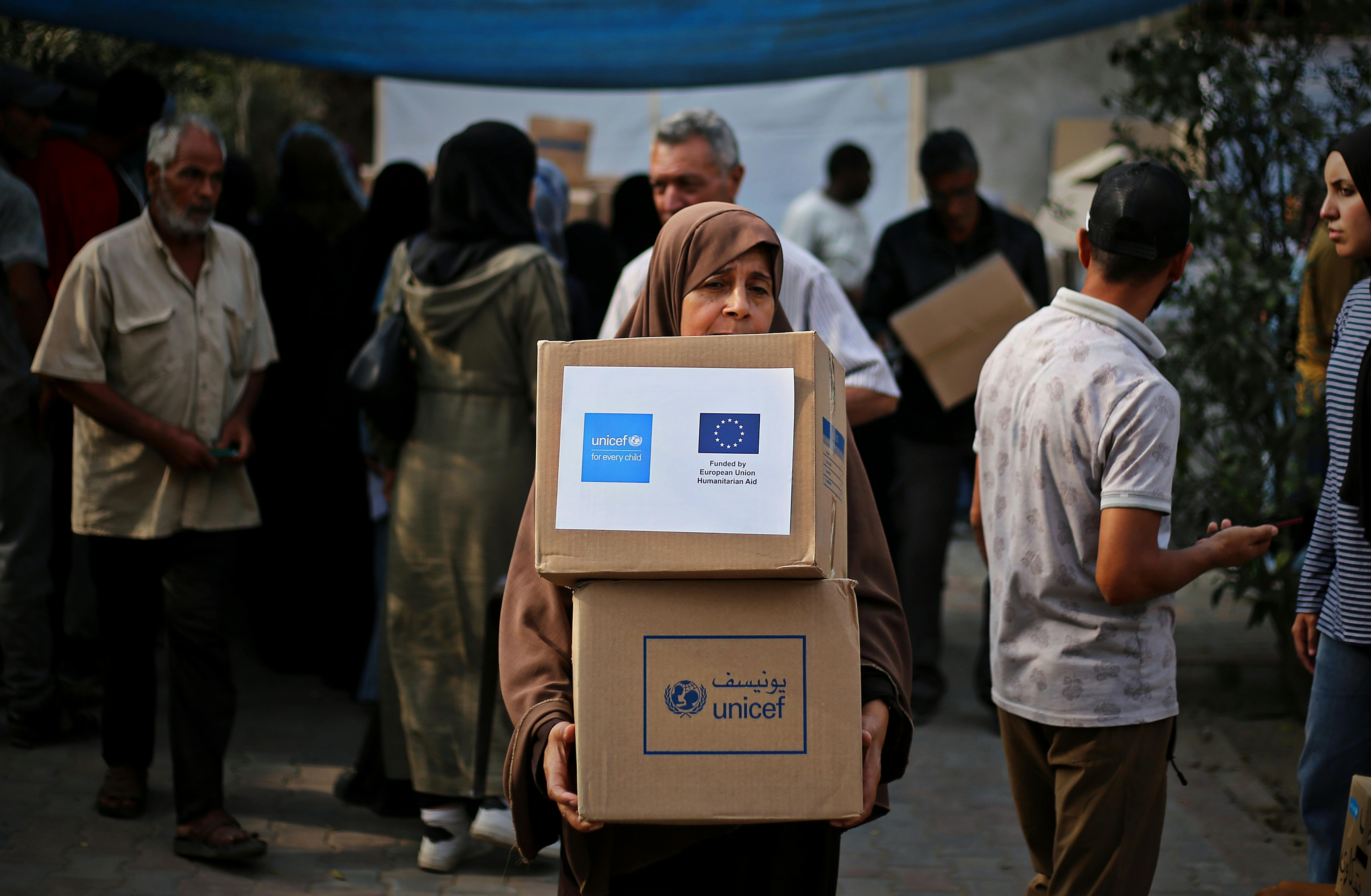 Una donna cammina con due pacchi ricevuti dall'UNICEF che contengono indumenti e coperte invernali, per sopravvivere al freddo intenso. Siamo a gaza, novembre 2025