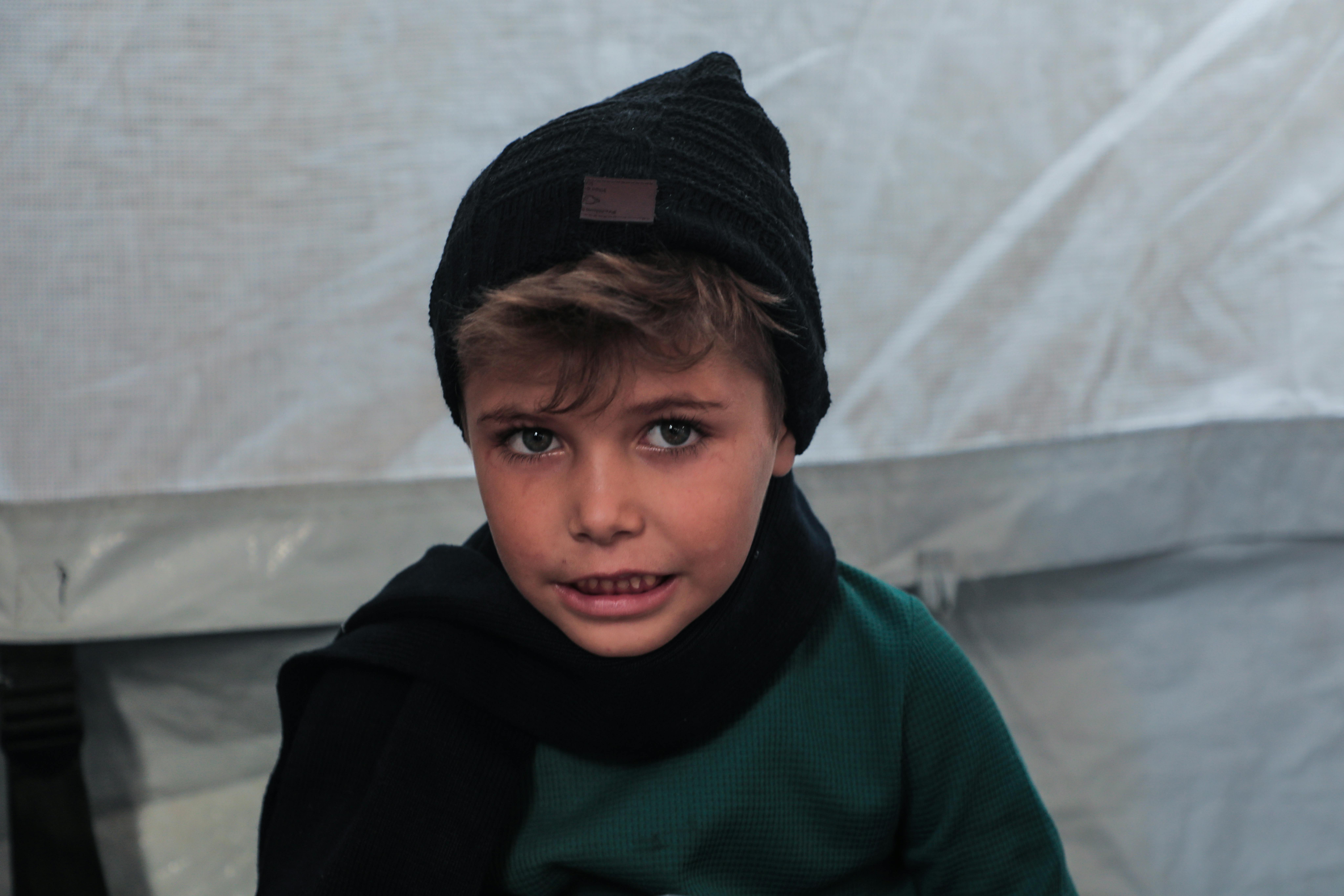 Distribuzione di abiti invernali per i bambini di Gaza City, il 12 novembre 2025, mentre le temperature iniziano a scendere. Un bambino indossa sciarpa e cappello