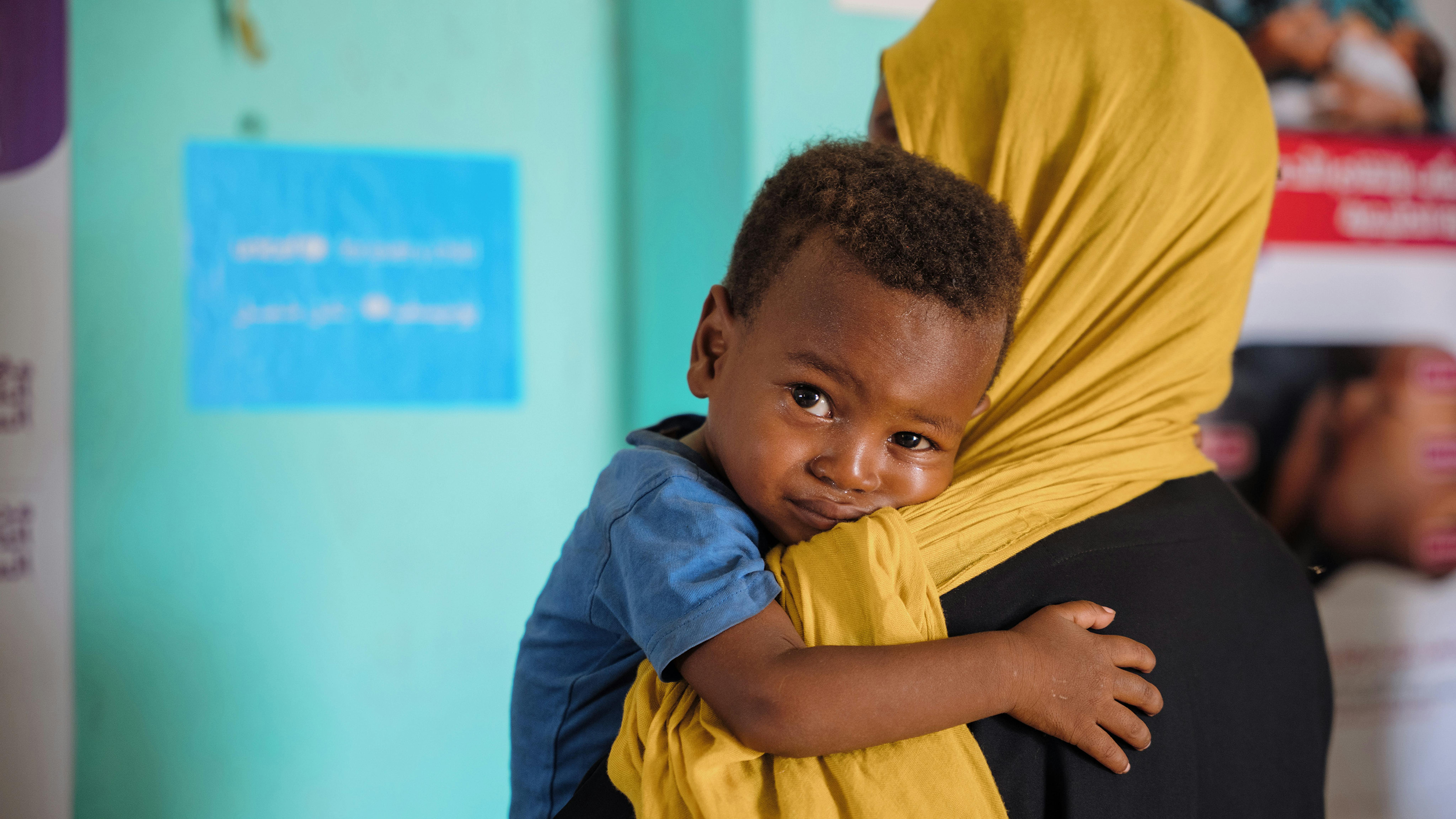 un ragazzino riposa sulla spalla del suo assistente mentre aspetta cure in una struttura sanitaria supportata dall'UNICEF presso il sito degli sfollati As-Senniya, Port Sudan