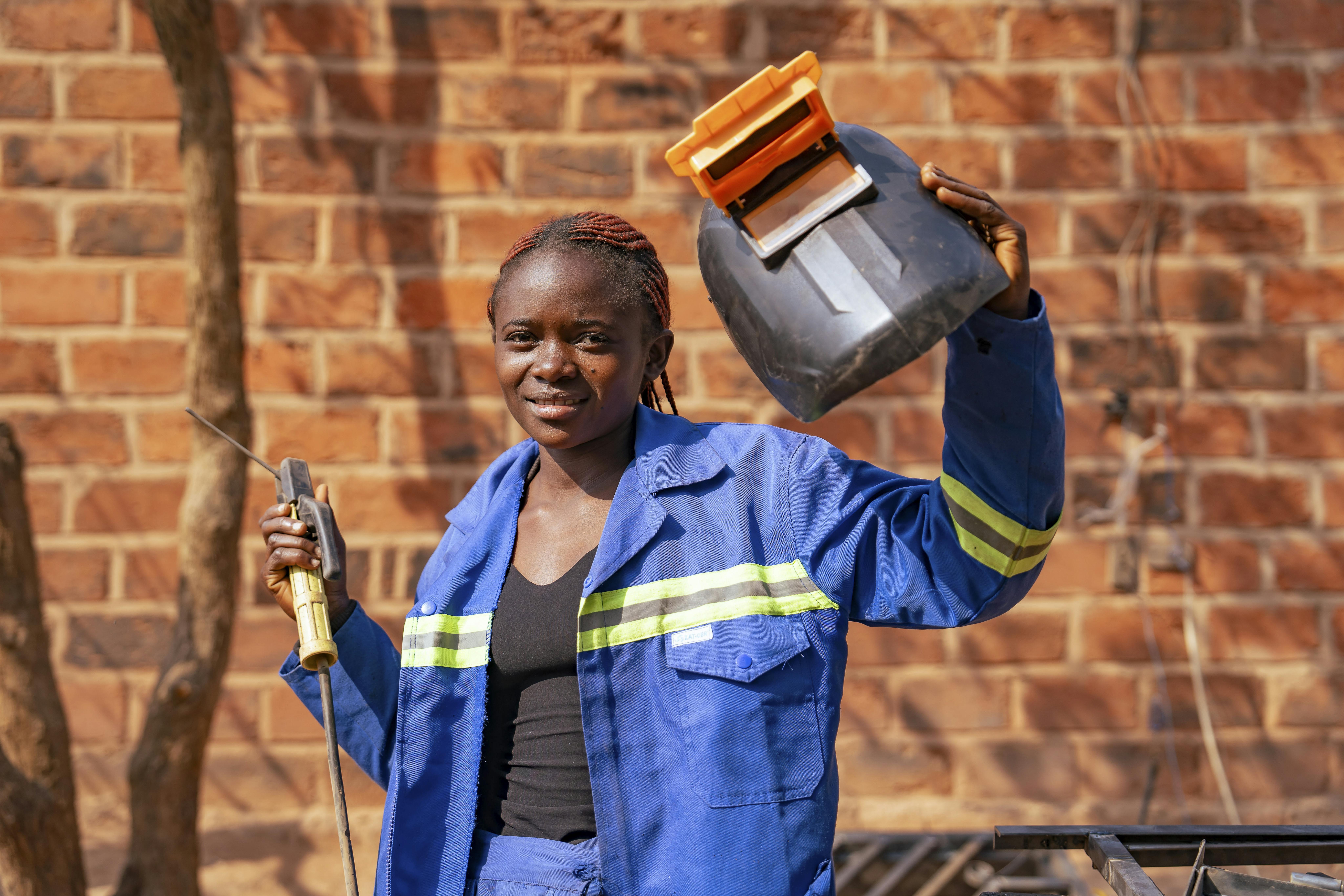 Astride, 16 anni, si trova nel cortile fuori dalla sua officina a Tshala e tiene in mano la cornice di una finestra che ha appena finito di saldare. Siamo in Repubblica Democratica del Congo, dove grazie a un percorso di formazione e aiuti in denaro a sua madre, sono riuscite ad uscire dalla povertà estrema