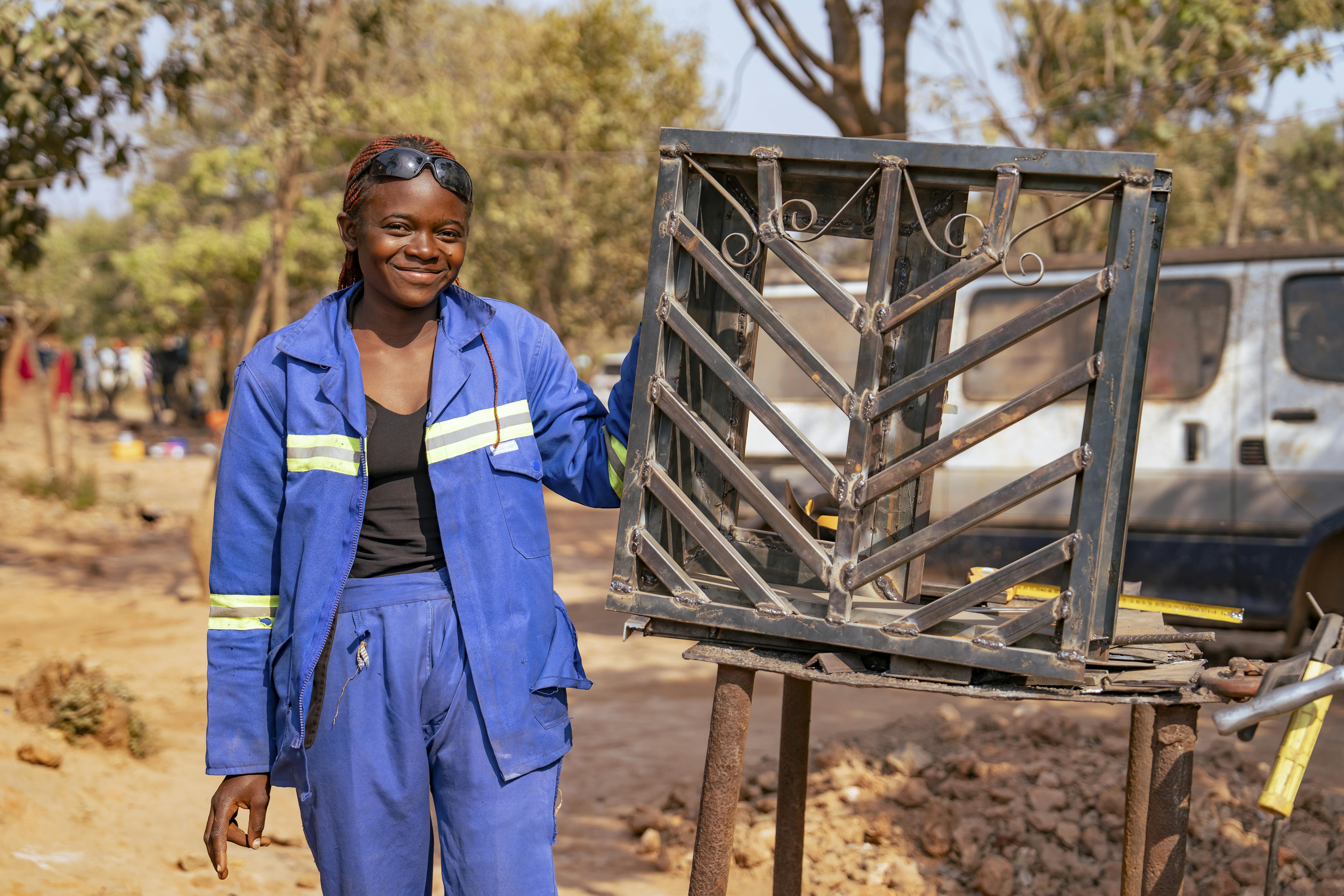 Astride mostra il suo lavoro di saldatura, nel cortile dell'officina dove lavora. Siamo in Repubblica Democratica del Congo