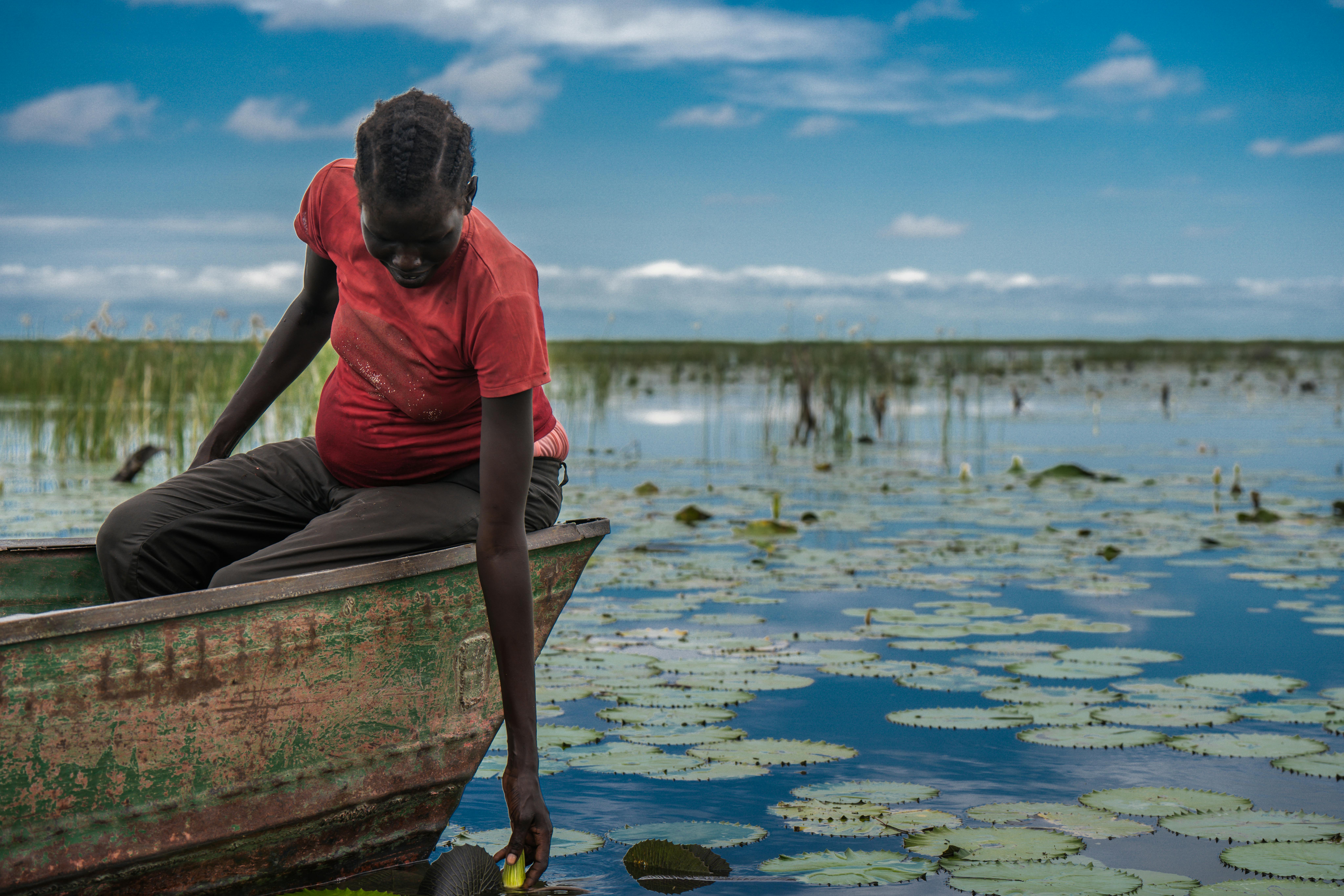 Sud Sudan: Nyawar, 30 anni, è seduta in una canoa tra i campi allagati vicino al campo profughi di Bentiu, in Sud Sudan. Dopo aver perso la casa e il bestiame a causa delle inondazioni, ora raccoglie ninfee per sfamare i suoi figli, una delle poche fonti di cibo ancora accessibili.