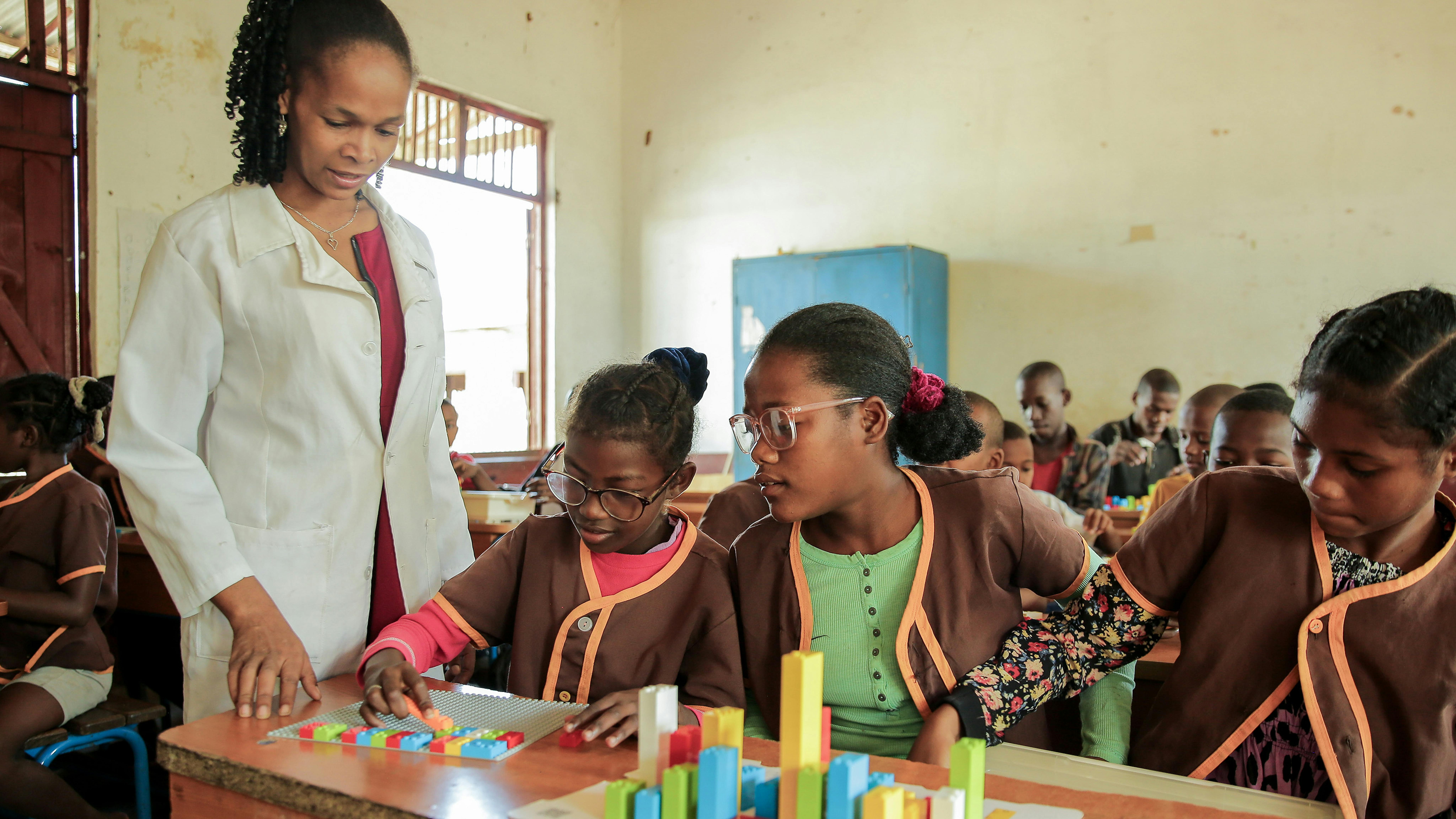 Due studentesse utilizzano mattoncini LEGO Braille a scuola, sotto la supervisione del loro insegnante. Siamo nella classe quinta della Impitiny Primary School, Farafangana, Regione di Fitovinany, Madagascar