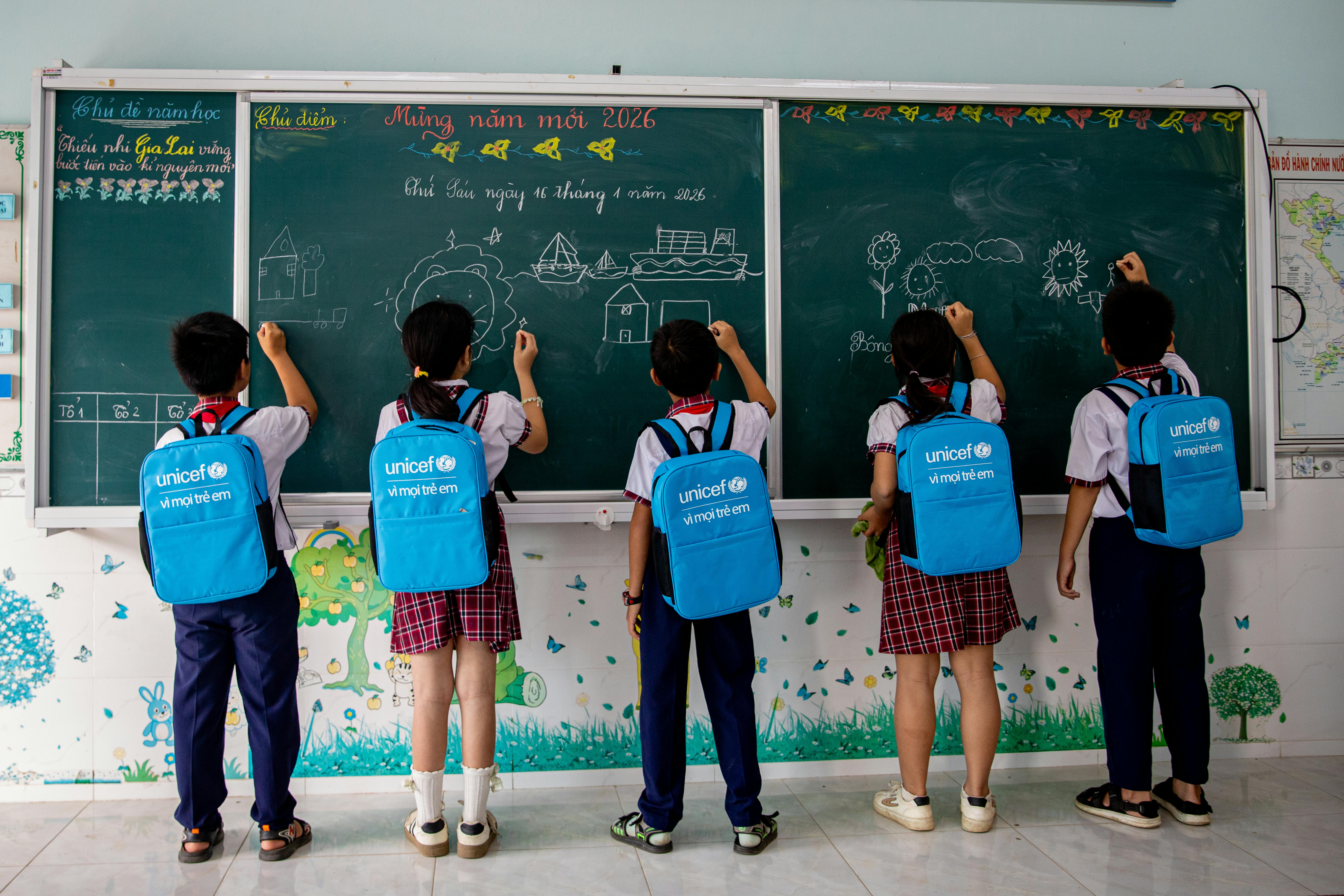 Da sinistra a destra: Đức, Quỳnh, Toàn, My, Trương – tutti di 10 anni – disegnano ciò che preferiscono sulla lavagna prima dell’inizio delle lezioni alla scuola primaria Phước Thắng II, mentre indossano gli zaini dell’UNICEF.