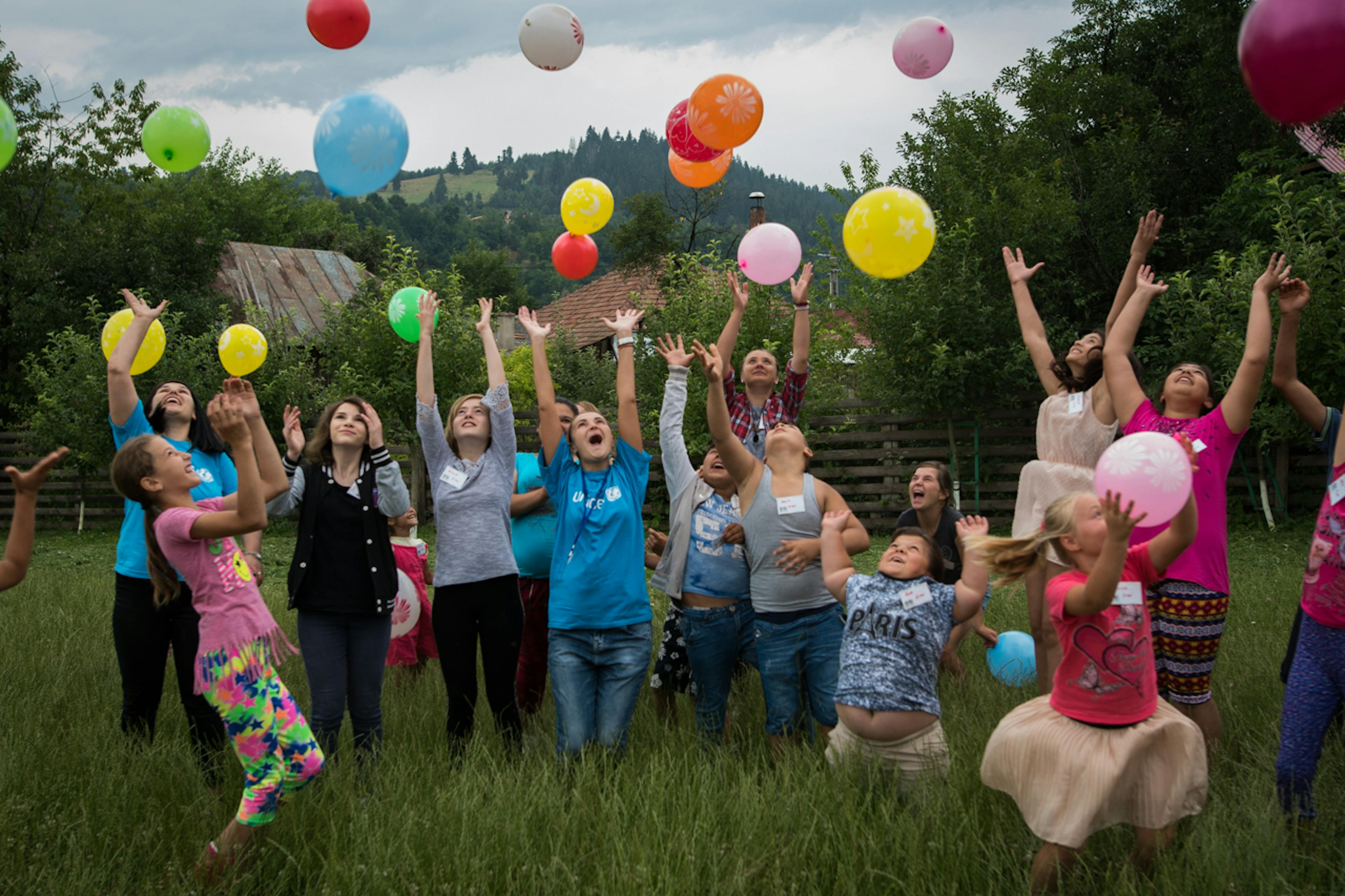 Bambini e ragazzi lanciano in aria palloncini, in un campo aperto