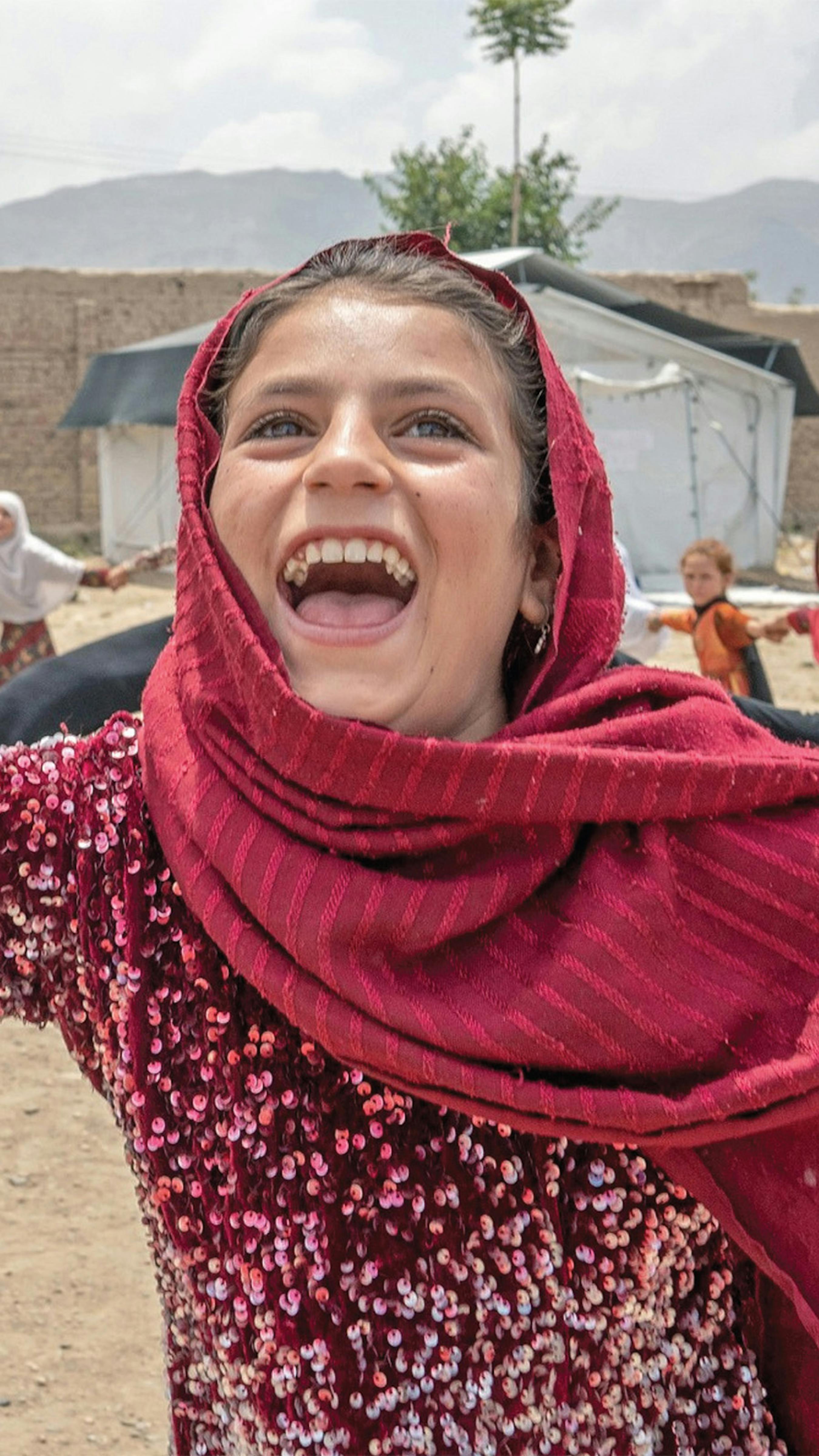Afghanistan, bambina sorride mentre fa il giro tondo con i suoi amici nel campo profughi