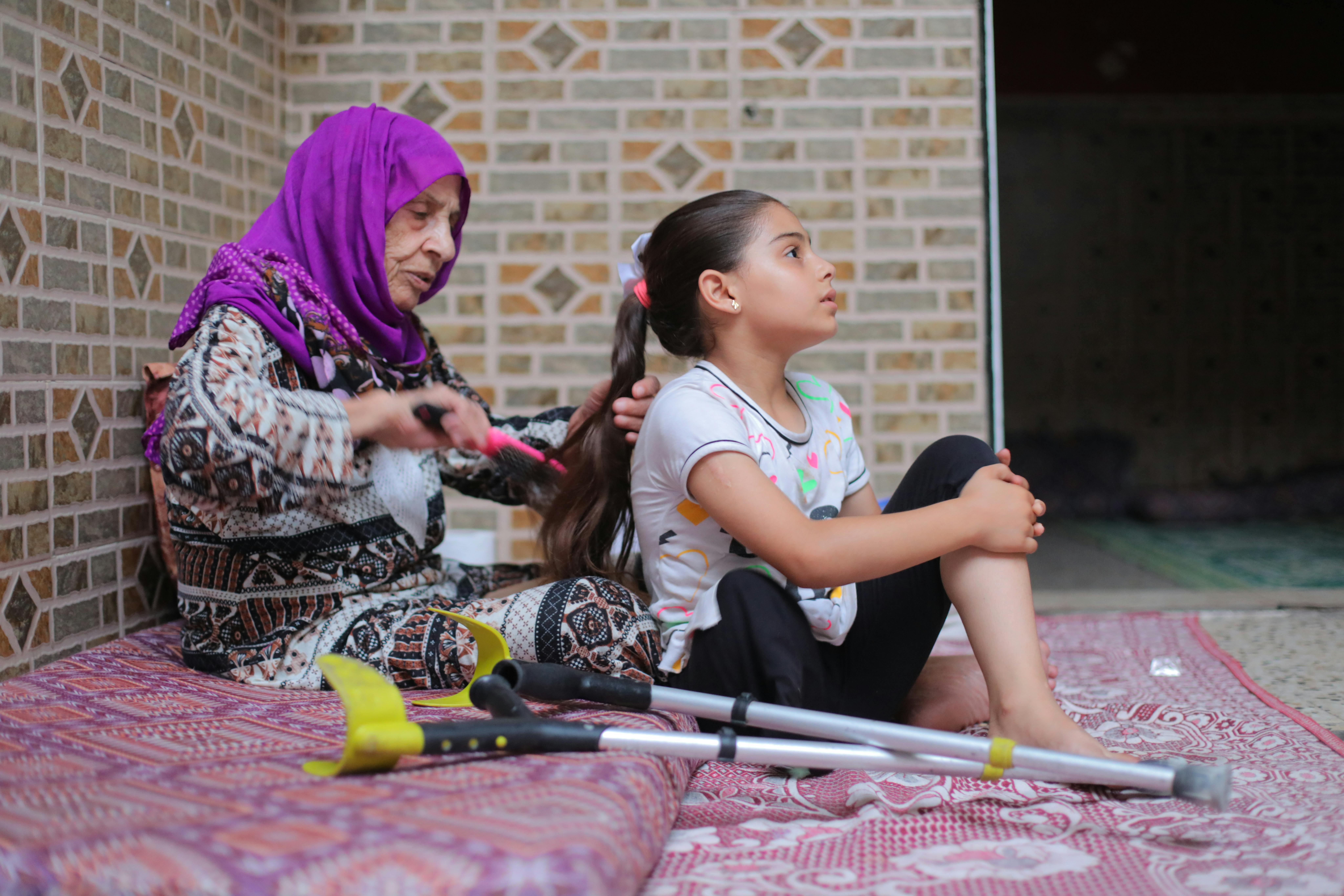 Meral viene pettinata da una donna nella casa dove è rifugiata a Nuseirat. Ha perso una gamba a causa dei bombardamenti nella Striscia di Gaza