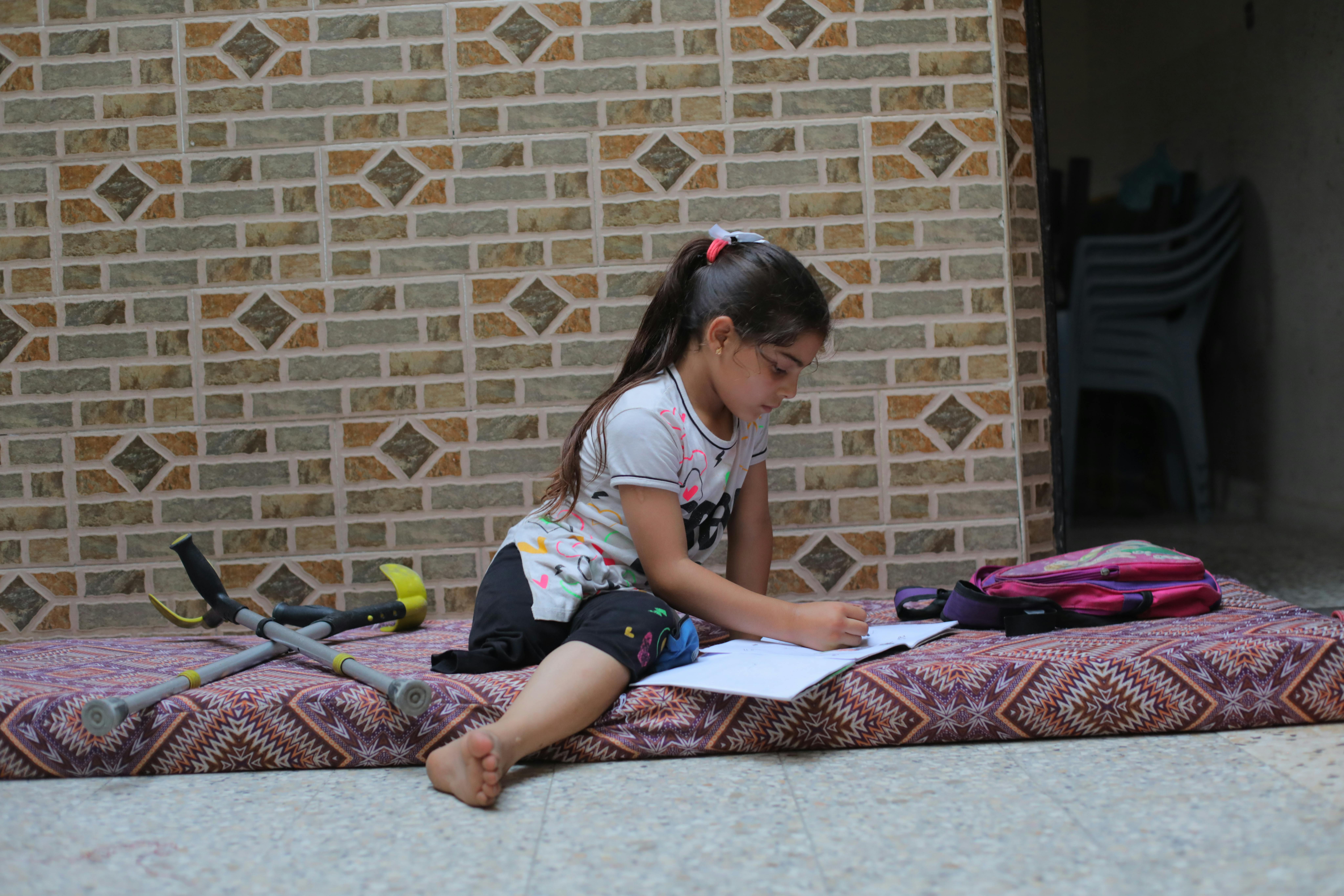 Meral Shukri Al-Babli, 9 anni, scrive su un materassino nella casa danneggiata dove si è rifugiata con il padre a Nuseirat. Ha perso una gamba a causa delle bombe, ora sogna di poter camminare