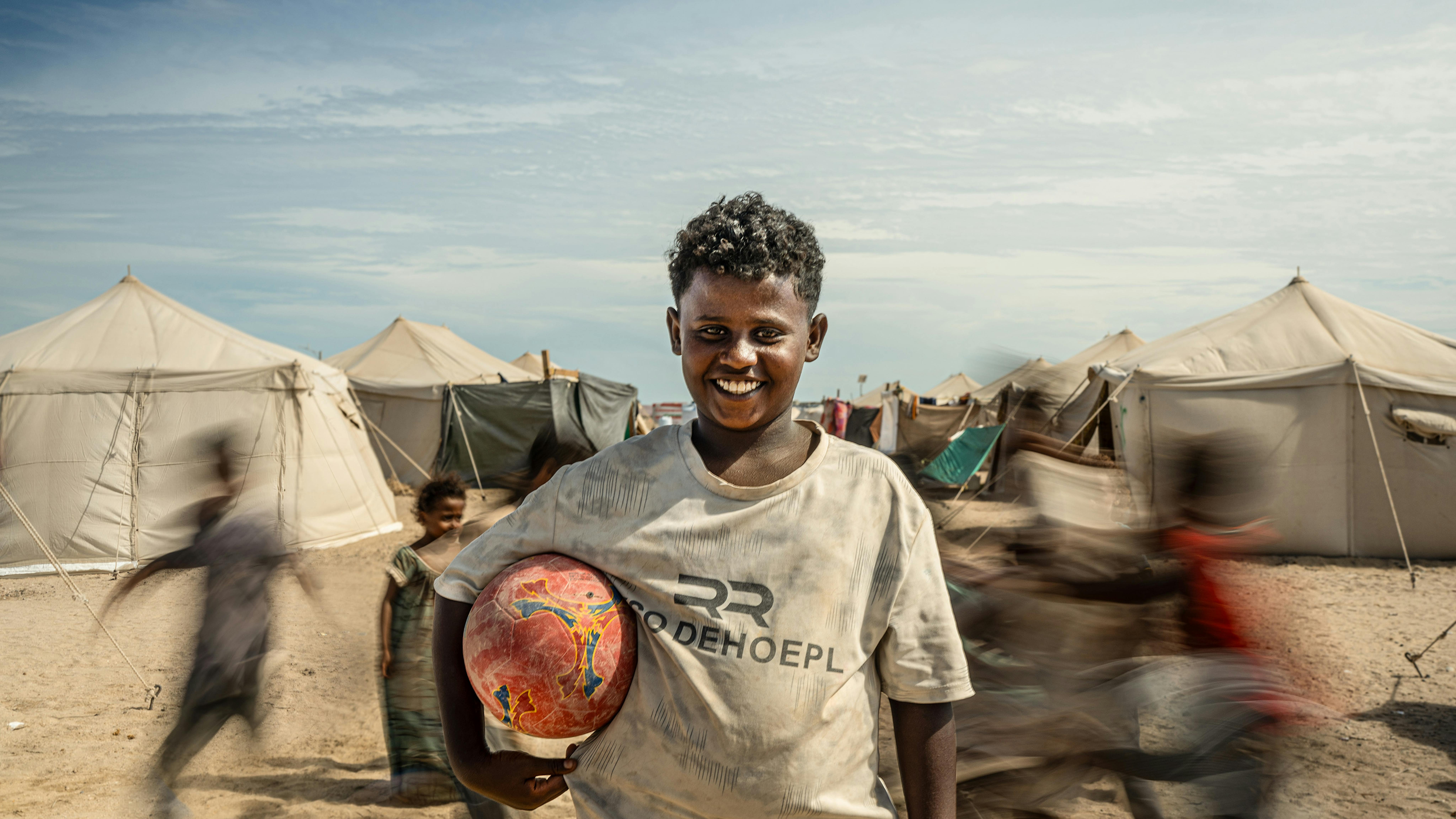 Bassam, 12 anni, tiene il suo pallone nel campo di Al-Firdous ad Aden. Sfollato da Al-Khokha, sogna di tornare a studiare e giocare. Questa testimonianza fa parte di una serie di interviste a due bambini, una madre e un padre sfollati dal conflitto in Yemen