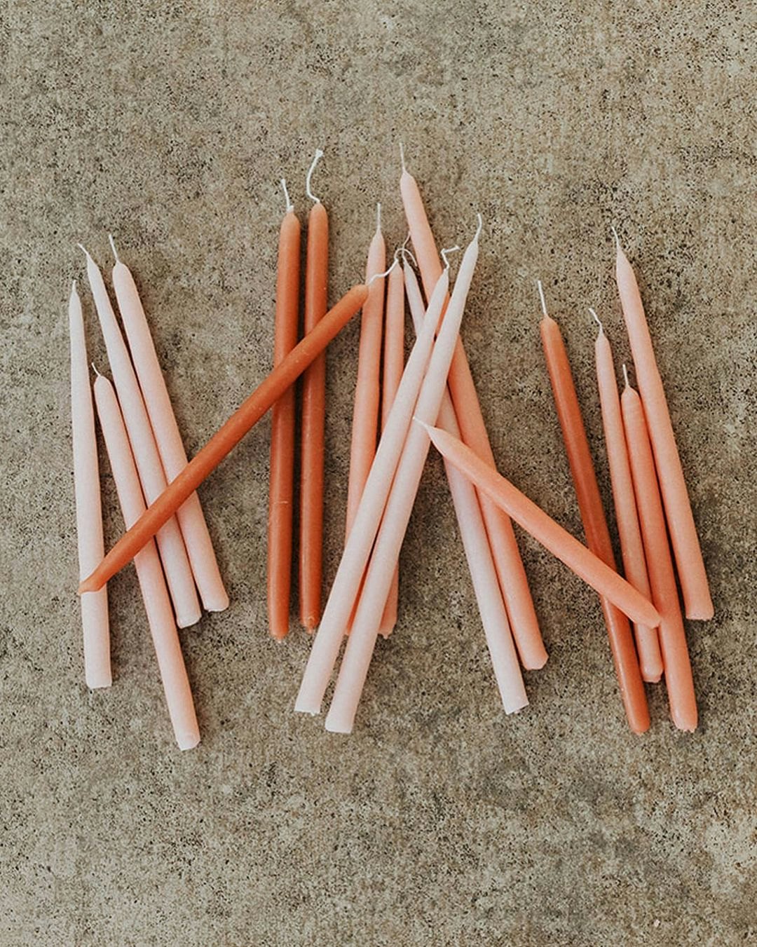 Pink, orange and tangerine coloured taper candles laying on a concrete floor 