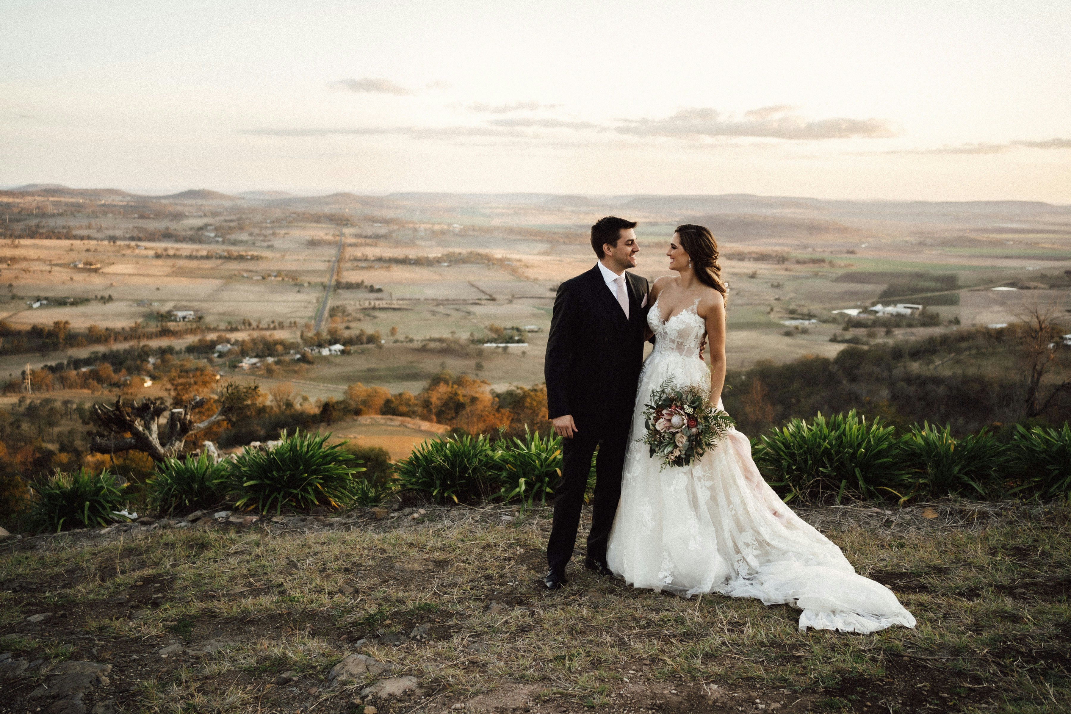 Bride and groom standing on escarpment edge looking at each other 