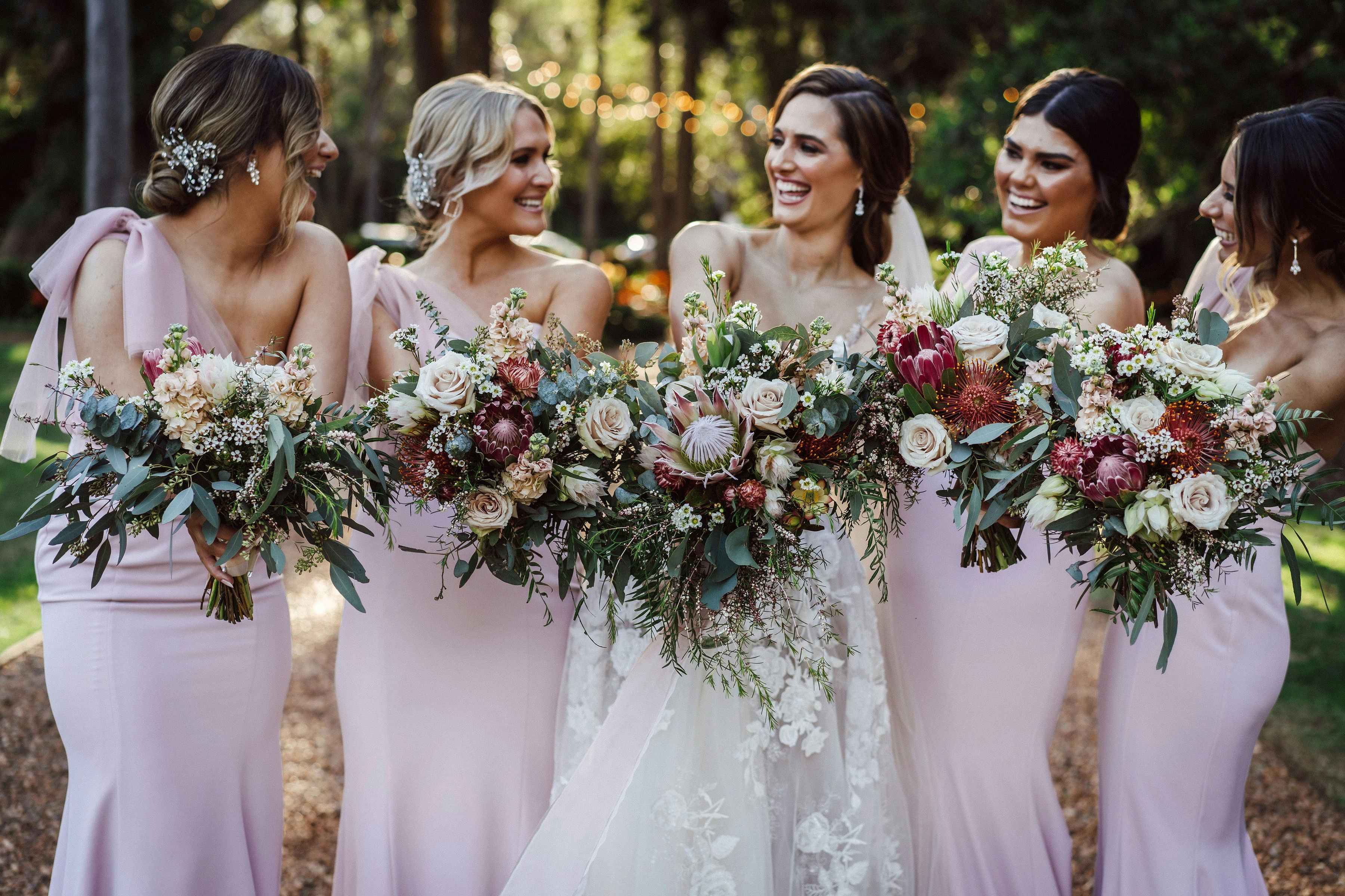 Bride and bridesmaids standing on driveway holding bouquets laughing