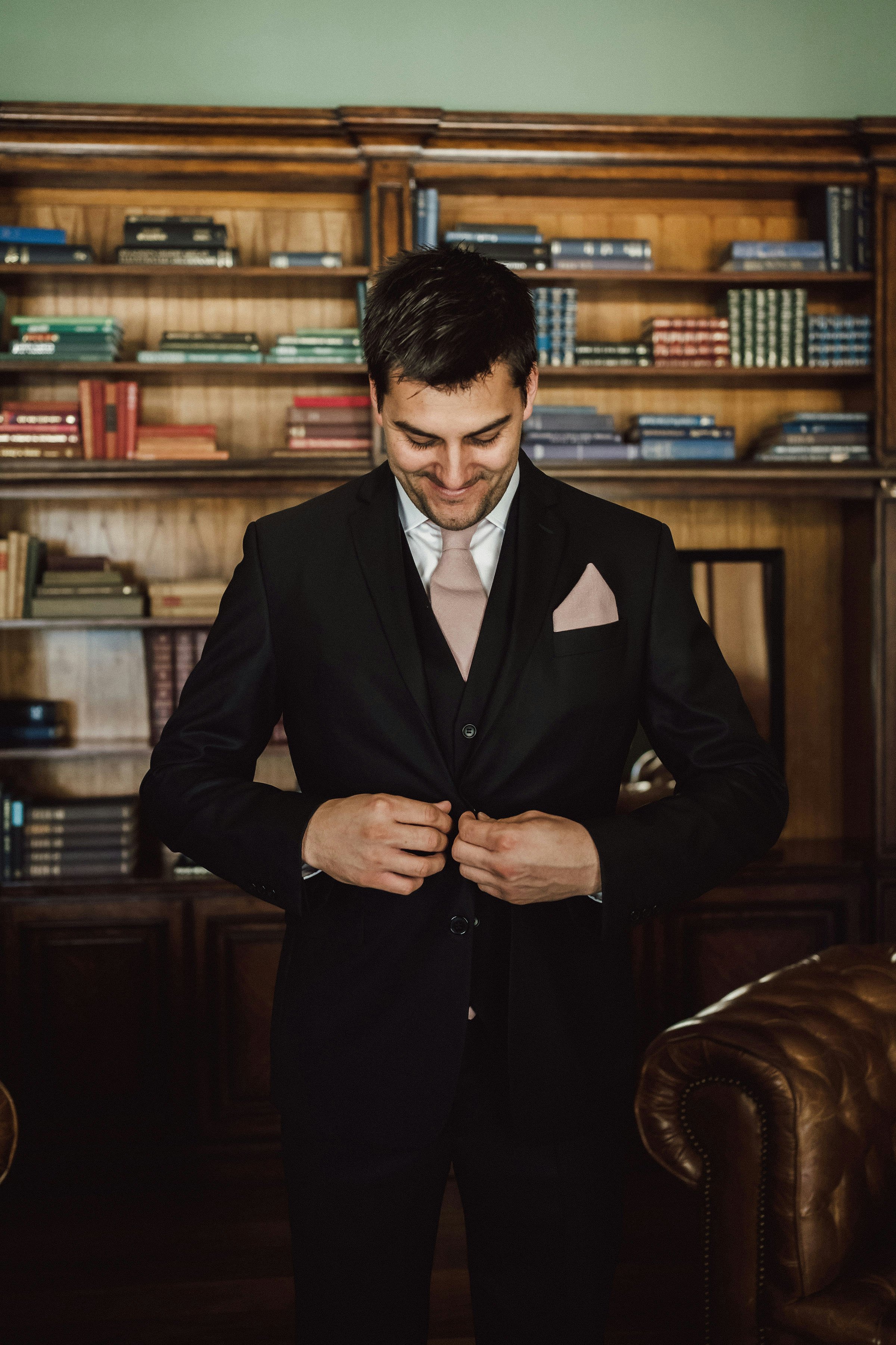Groom doing jacket button up in library 