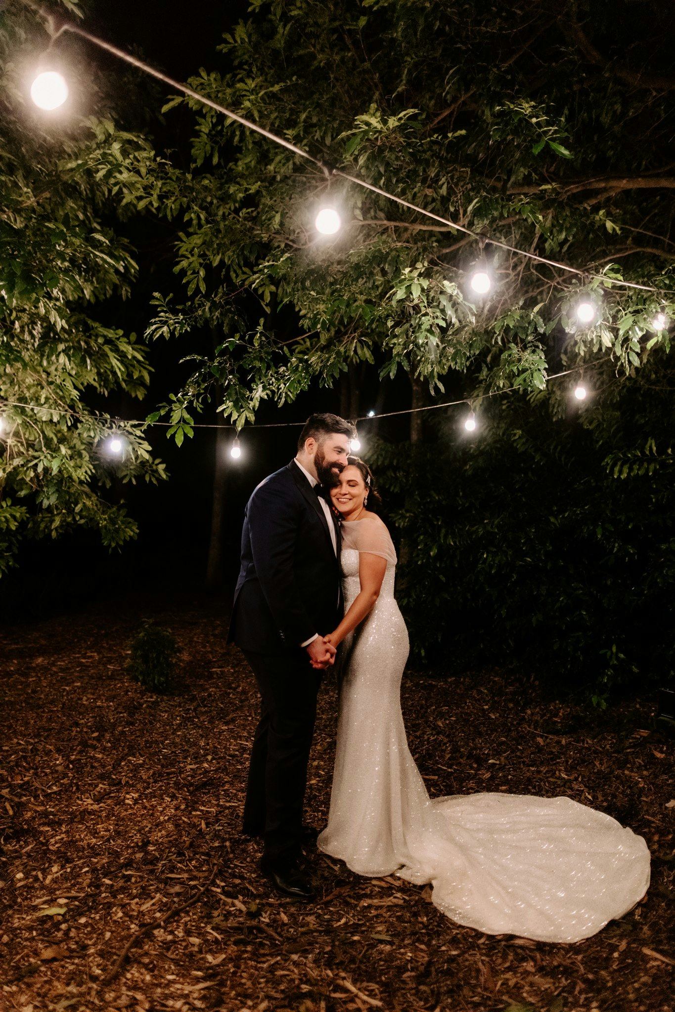 Bride and groom standing under festoon lights at night 