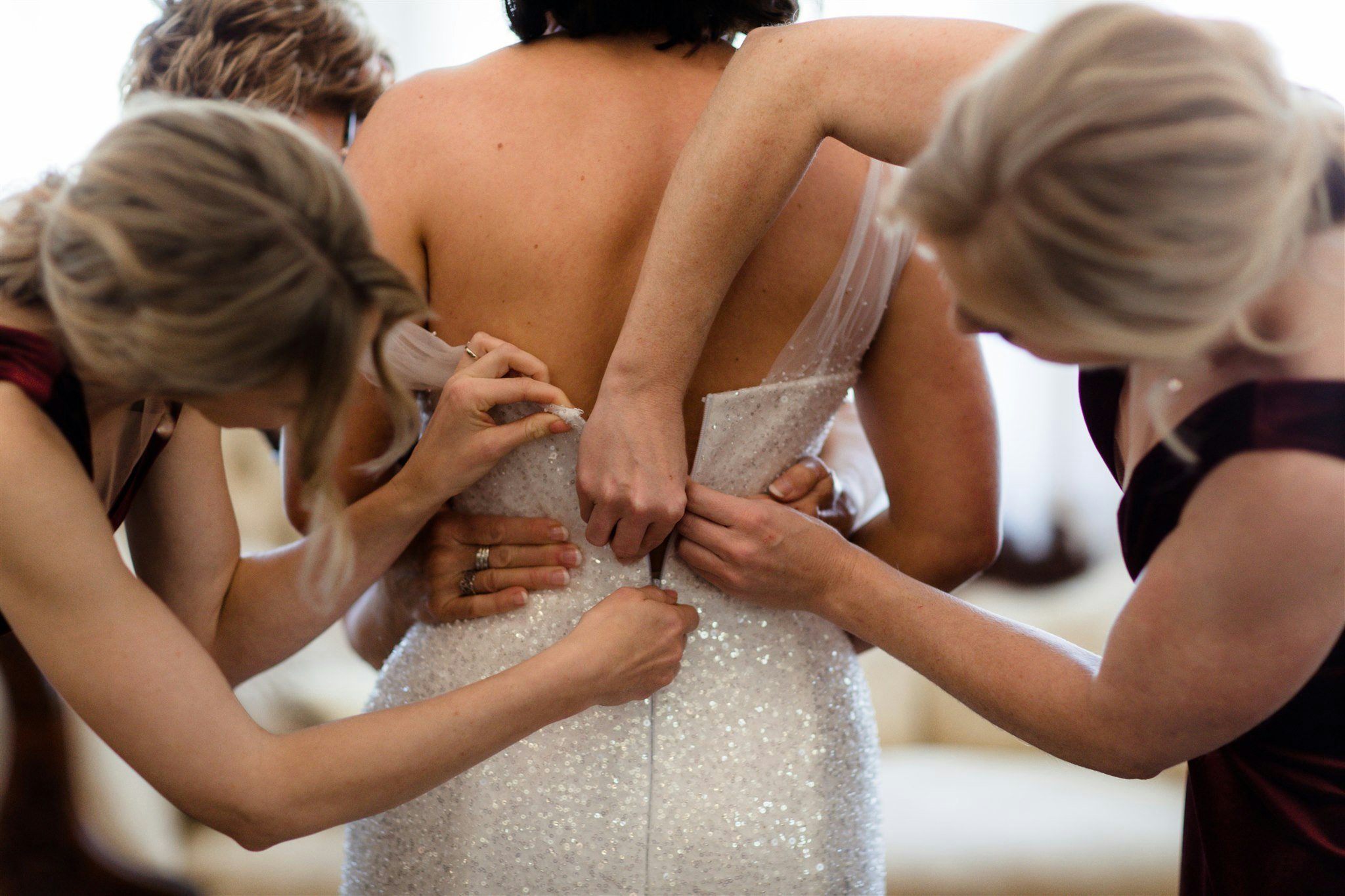 Bridesmaids zipping up brides dress 