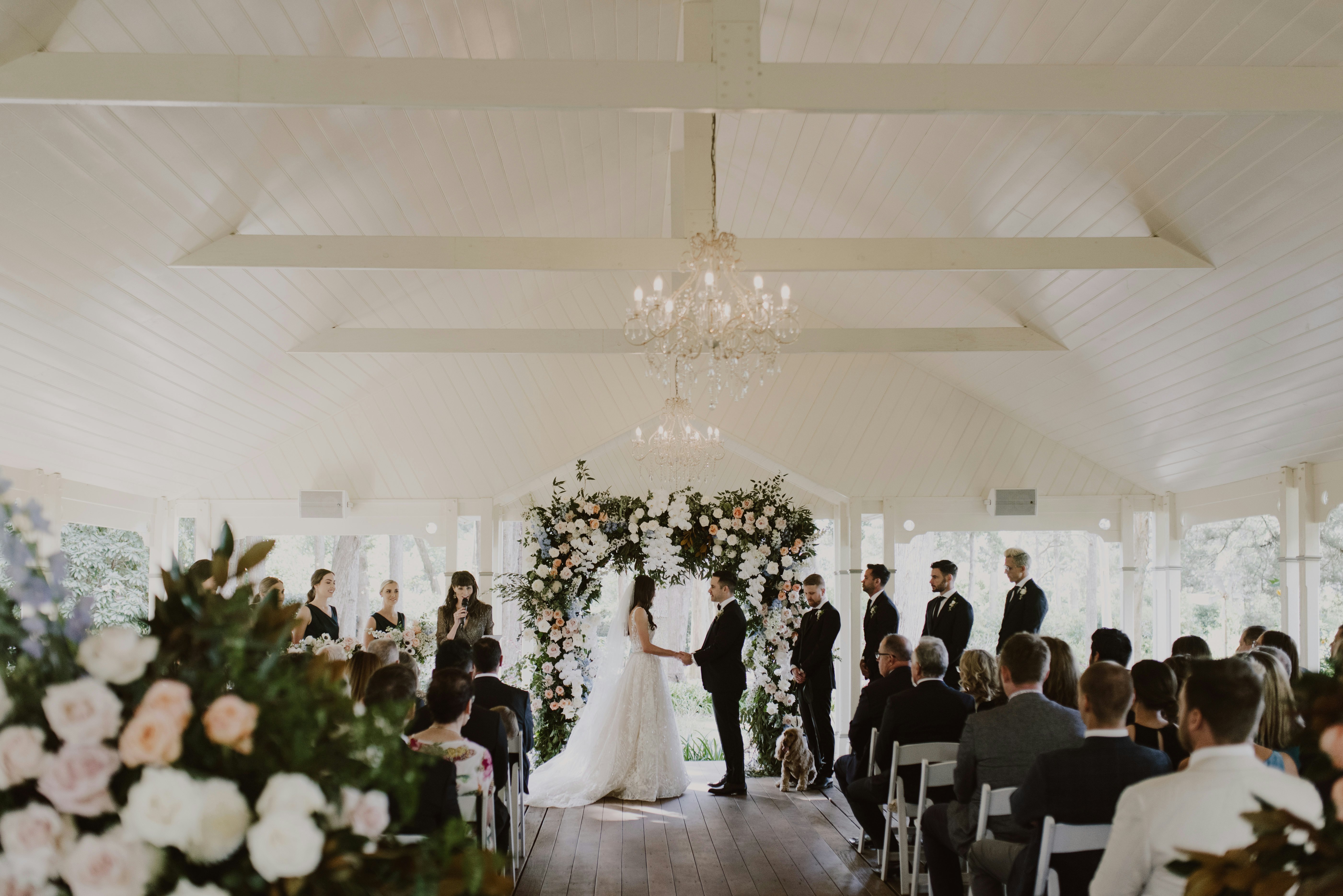 Photo of wedding ceremony with bride and groom standing in front of floral arbor 