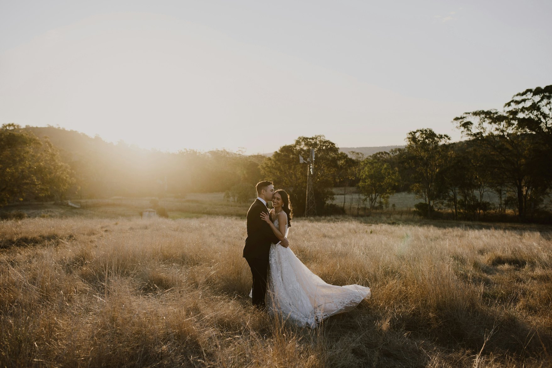 Bride and groom standing in field kissing 
