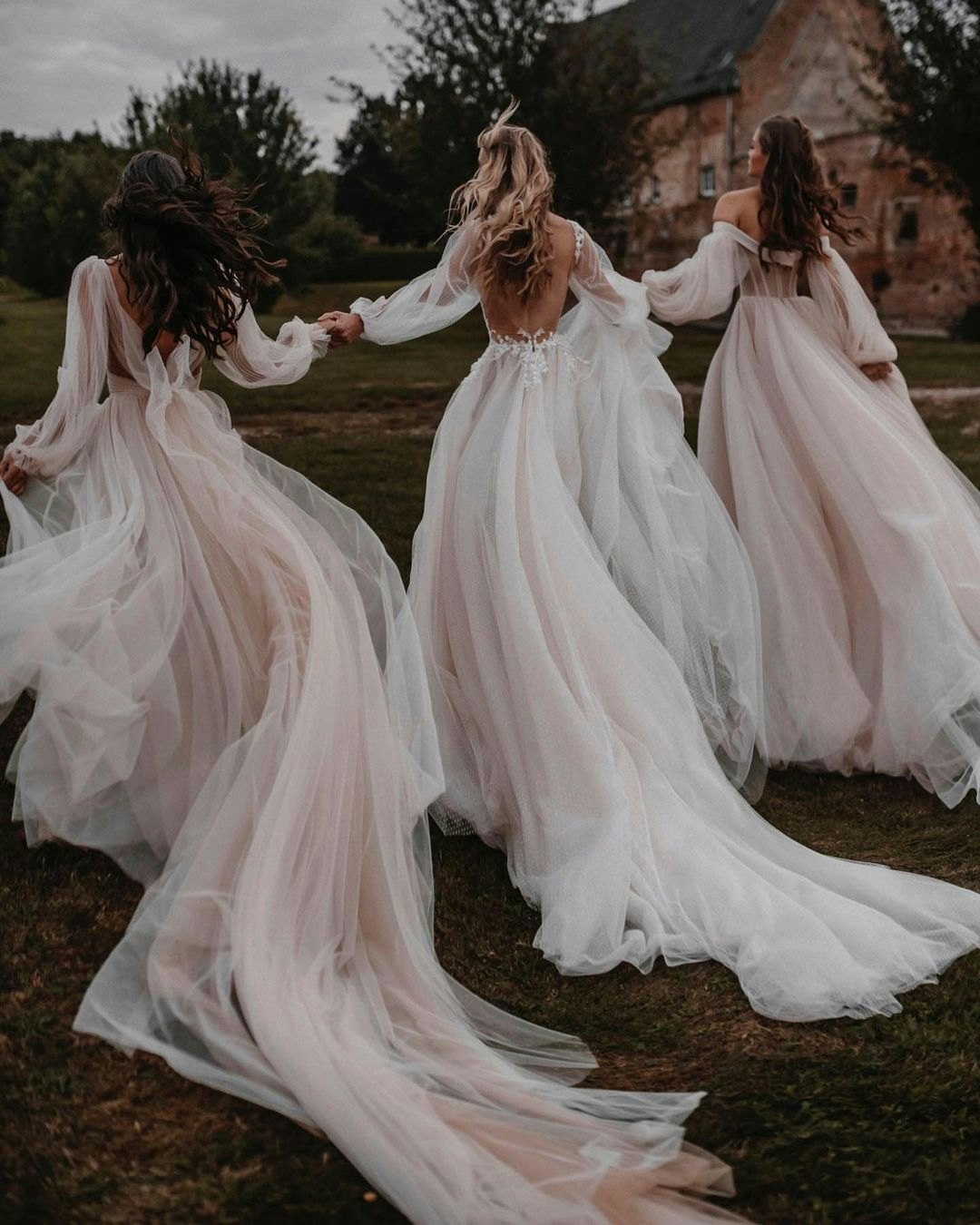 3 brides wearing dresses with long flowing trains 