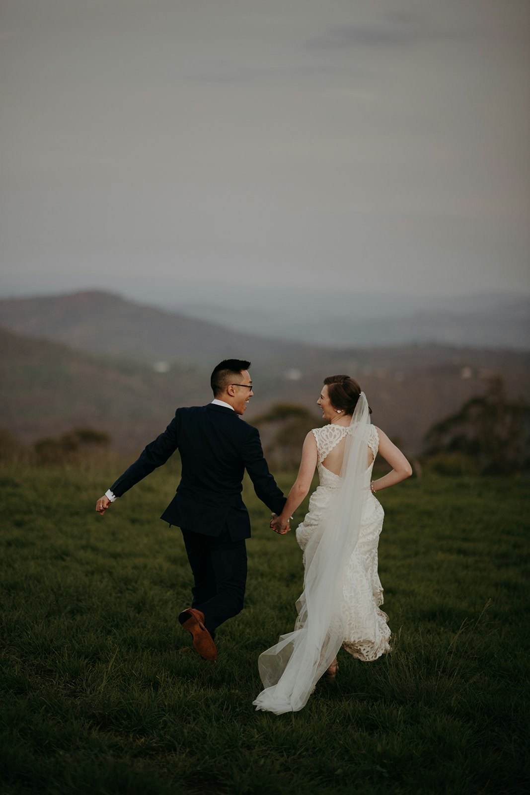 Bride and groom running through fields
