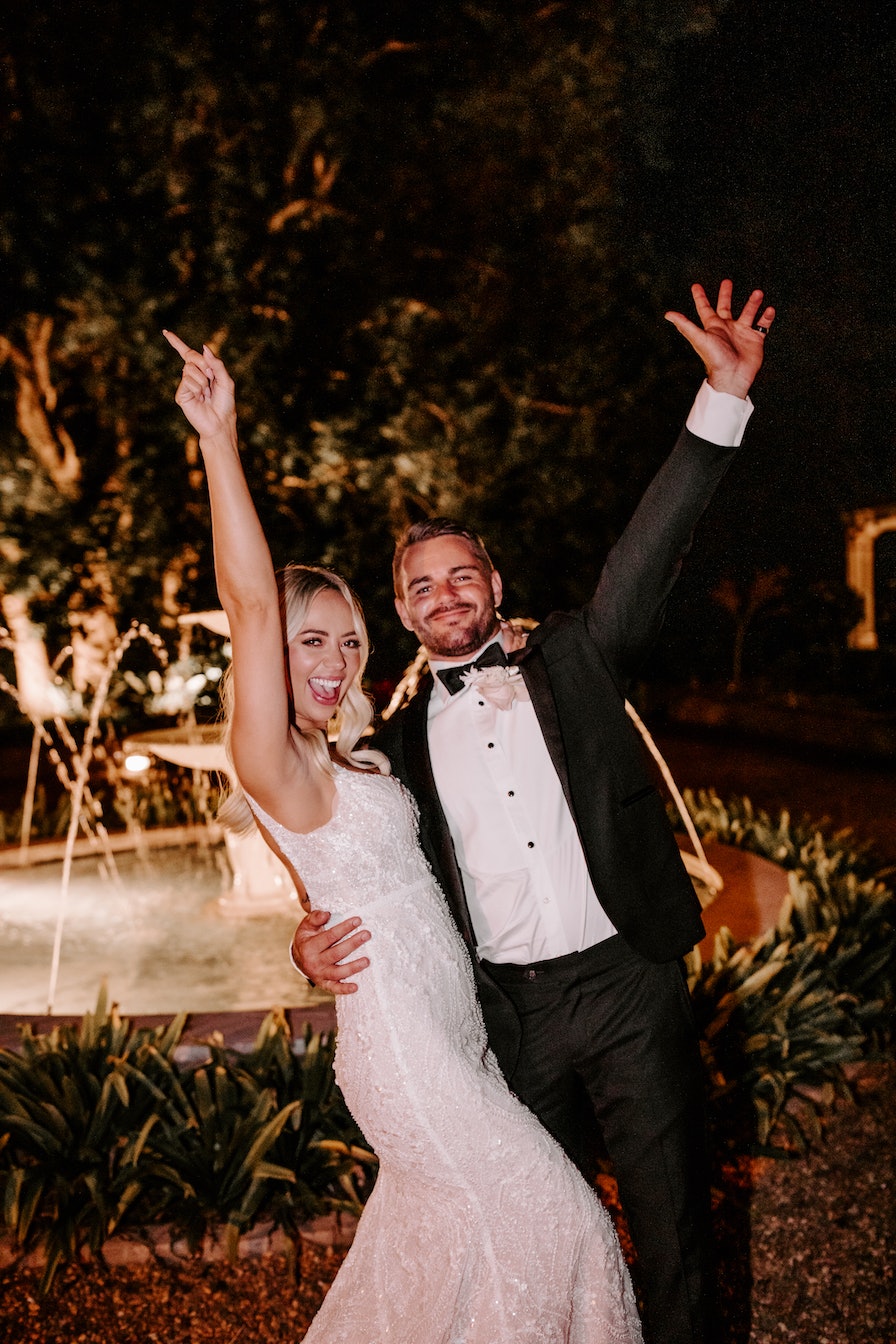 Bride and groom waving in front of fountain