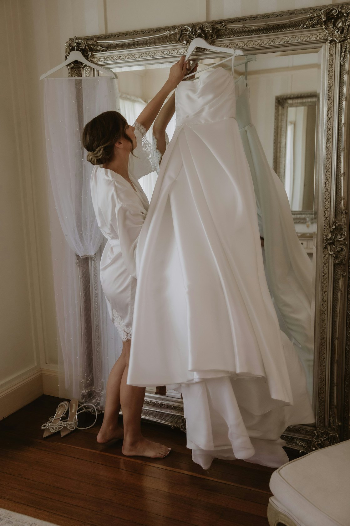 Bride hanging wedding dress on mirror 