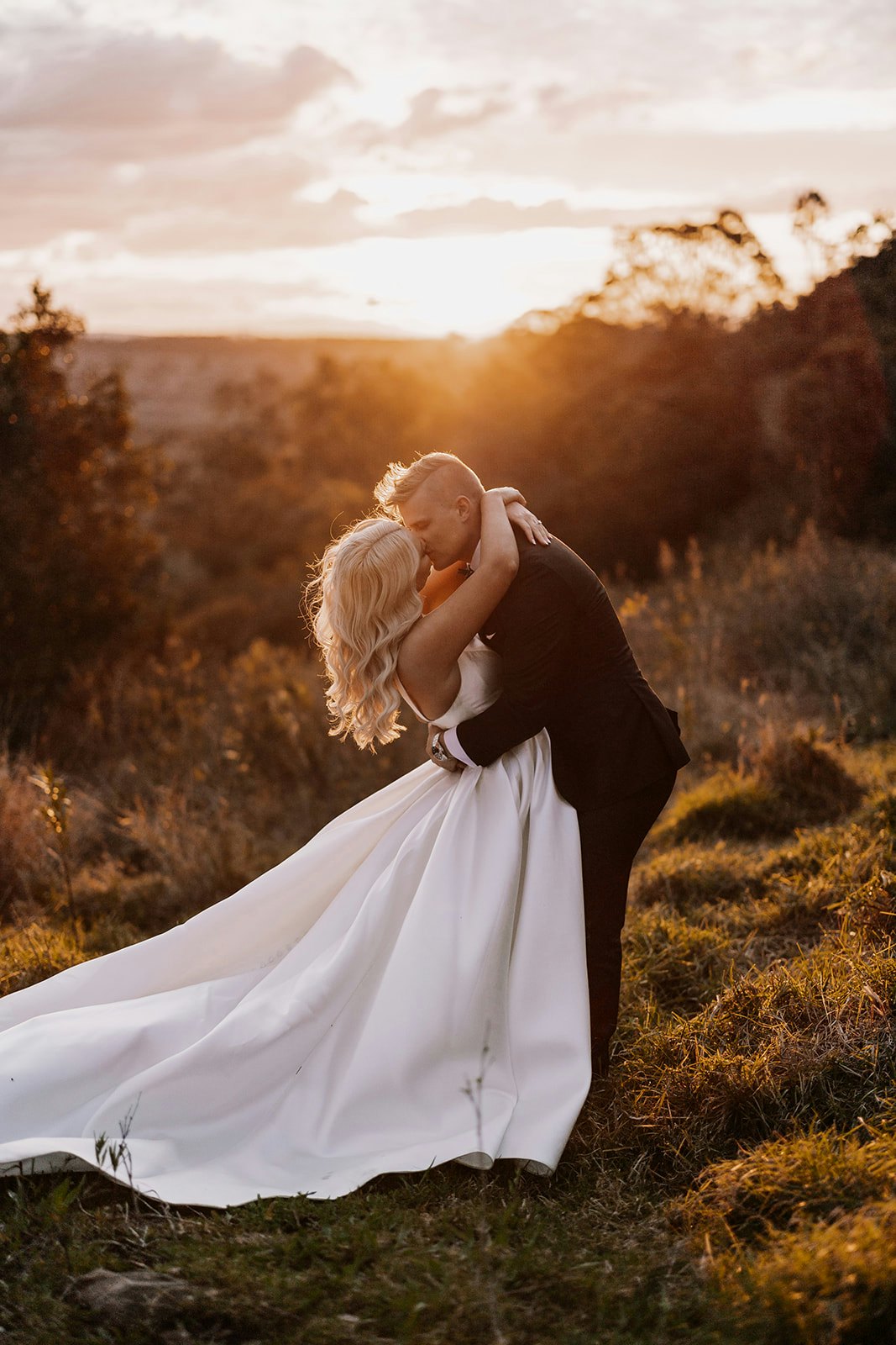 Bride and groom kissing in front of sunset