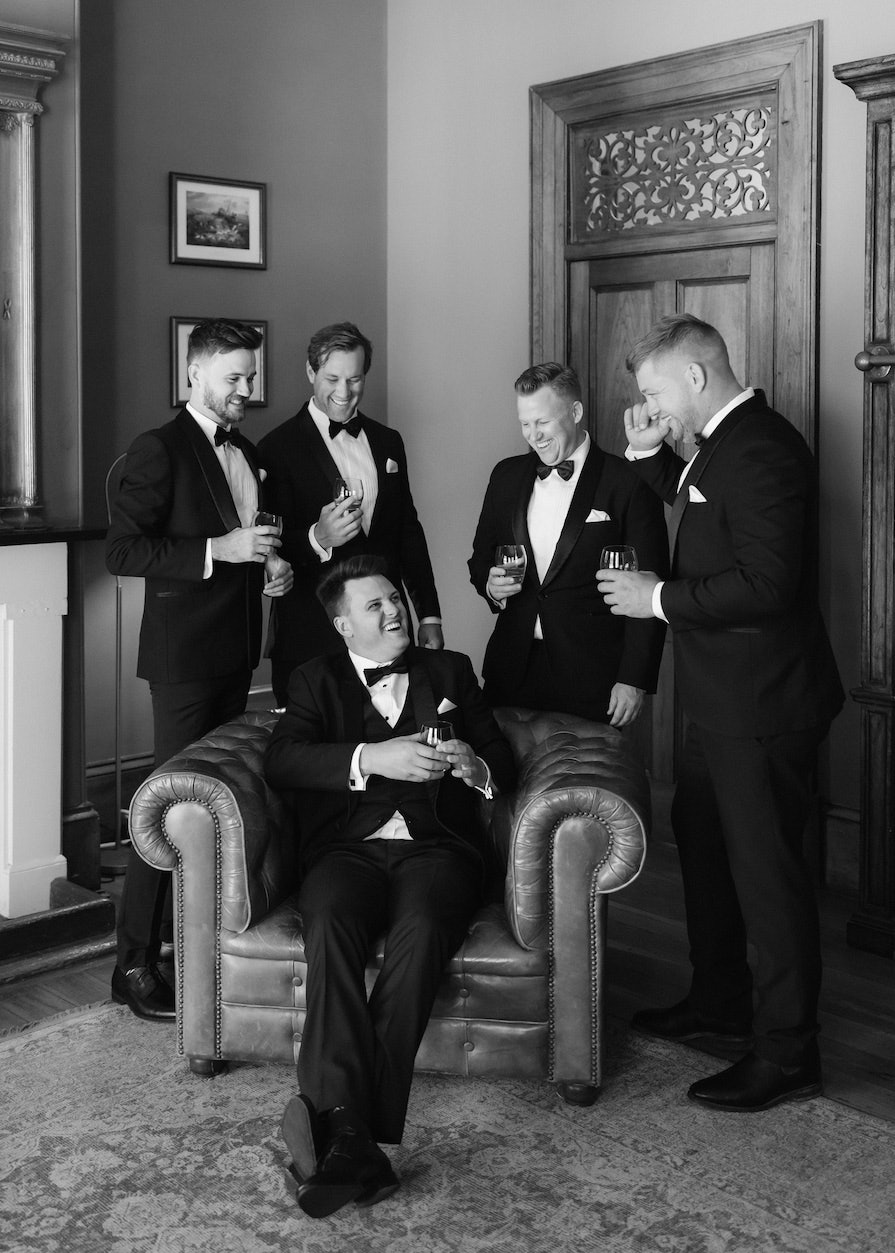 Groom and groomsmen drinking scotch in chairs