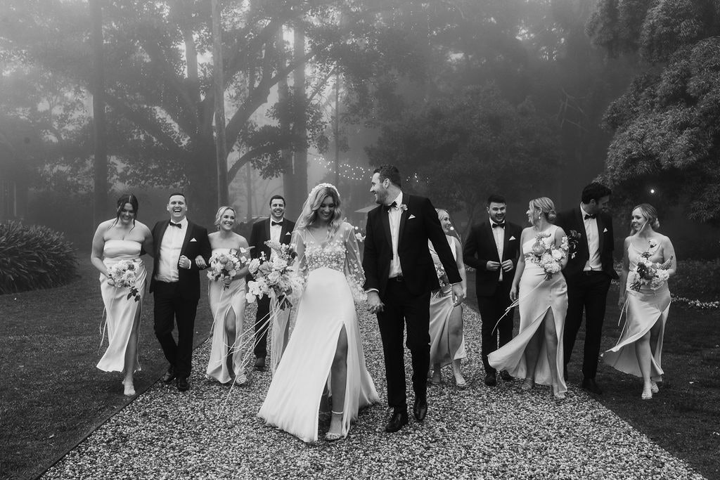 Bride and groom walking down driveway with wedding party