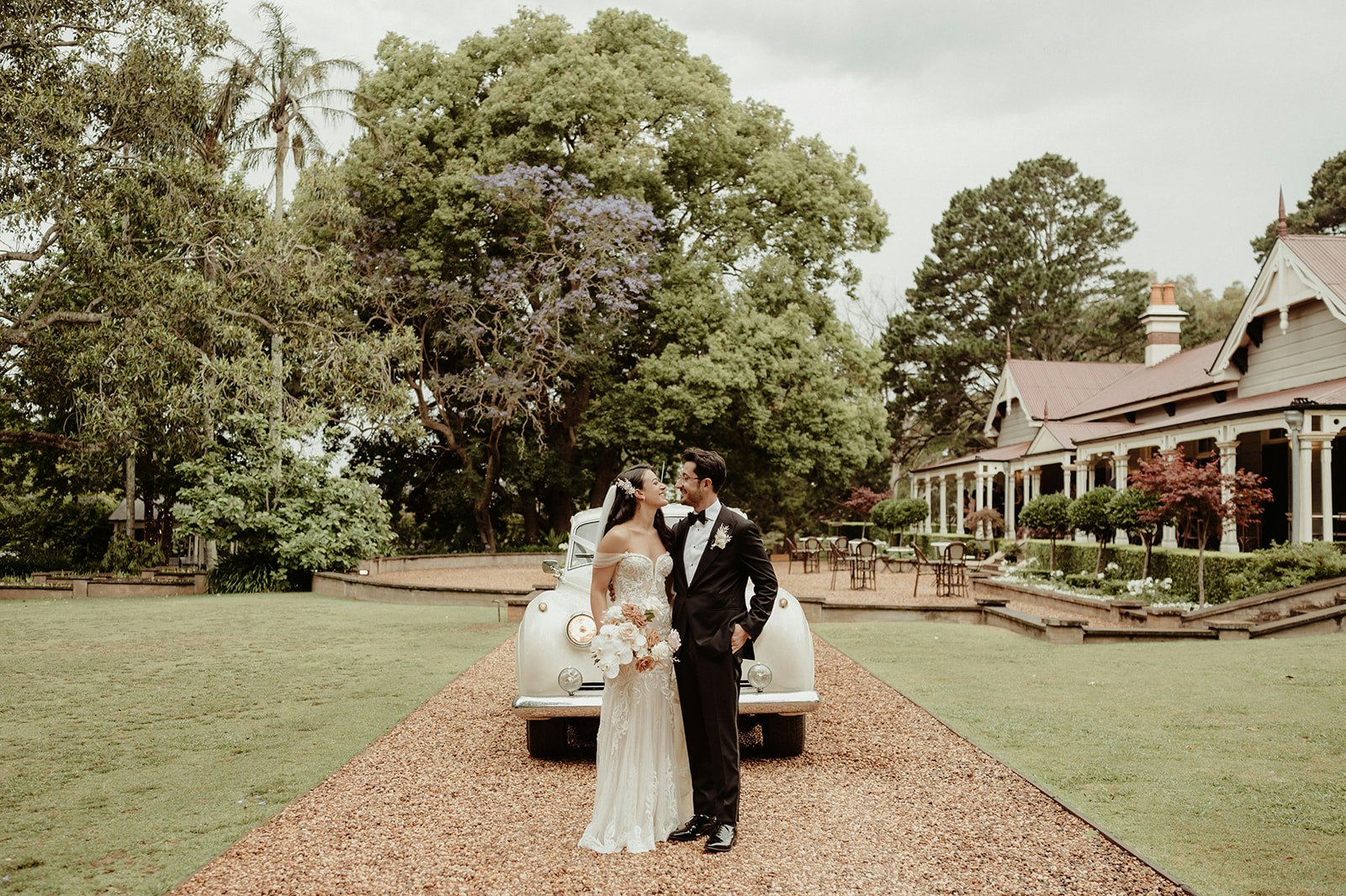 Bride and groom standing in front of car and homestead