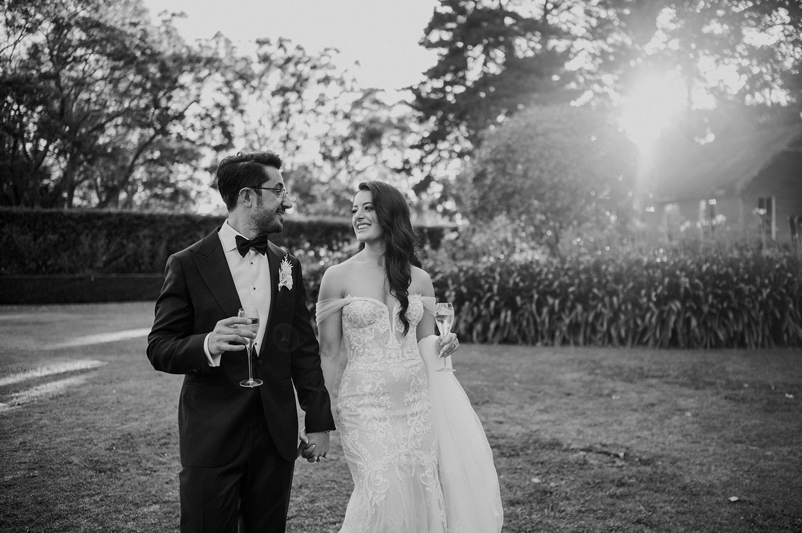 Bride and groom holding champagne glass walking through gardens
