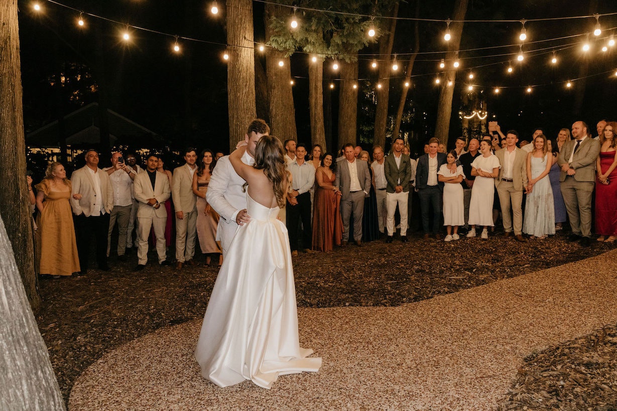 Bride and groom dancing outside under festoon lights