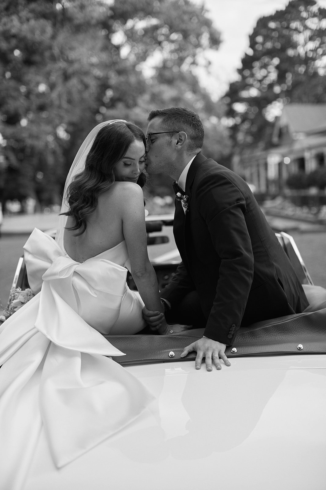 Bride and groom kissing on car