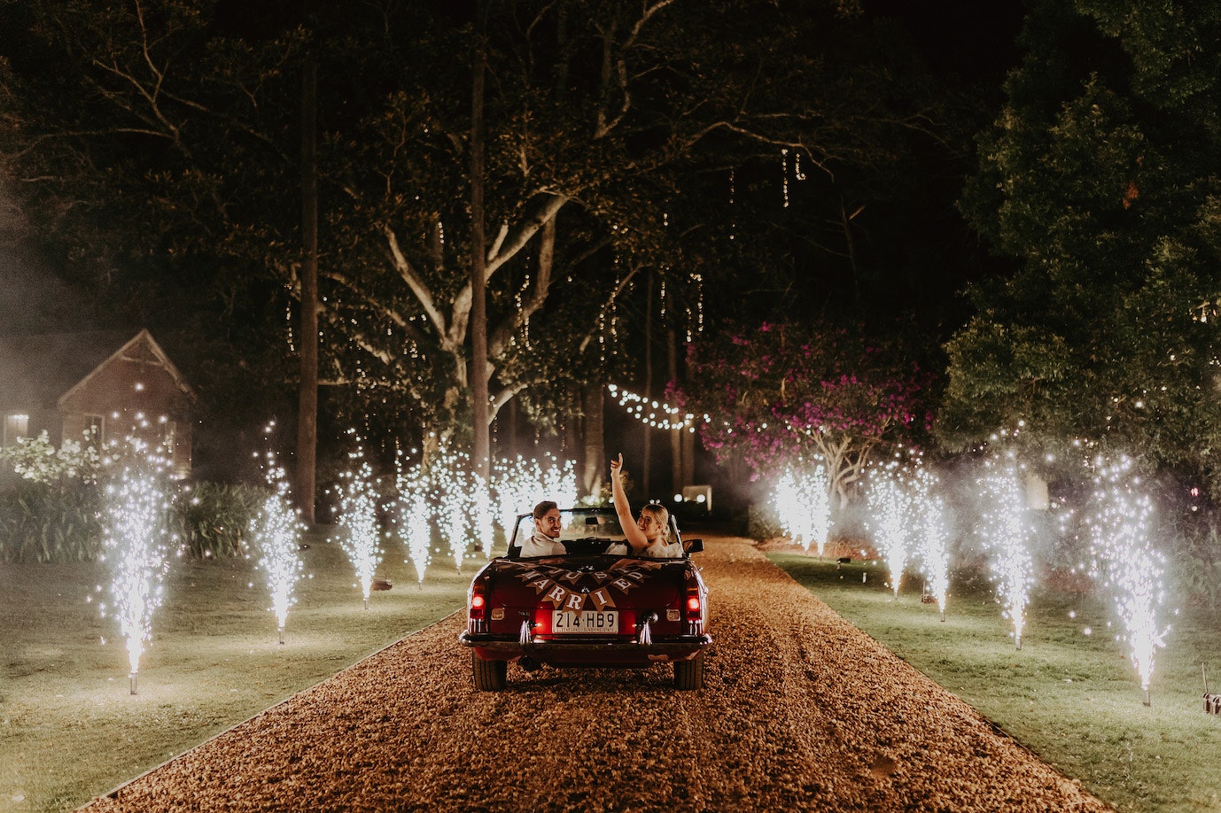 Bride and groom driving off in car with fireworks