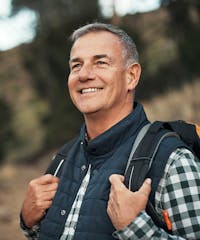 smiling man with backpack on his shoulders in the woods
