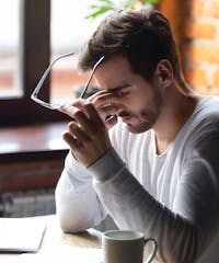 Male sitting at a coffee shop taking off his glasses and rubbing his eyes