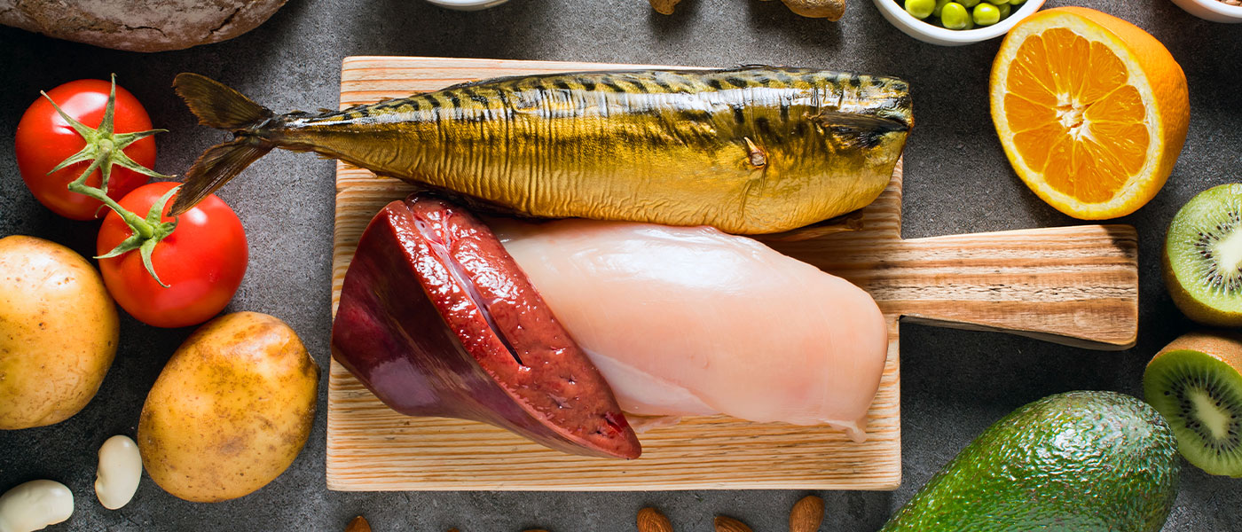 Healthy food on a cutting board. Fish, liver and chicken with healthy fruits and vegetables surrounding them. 