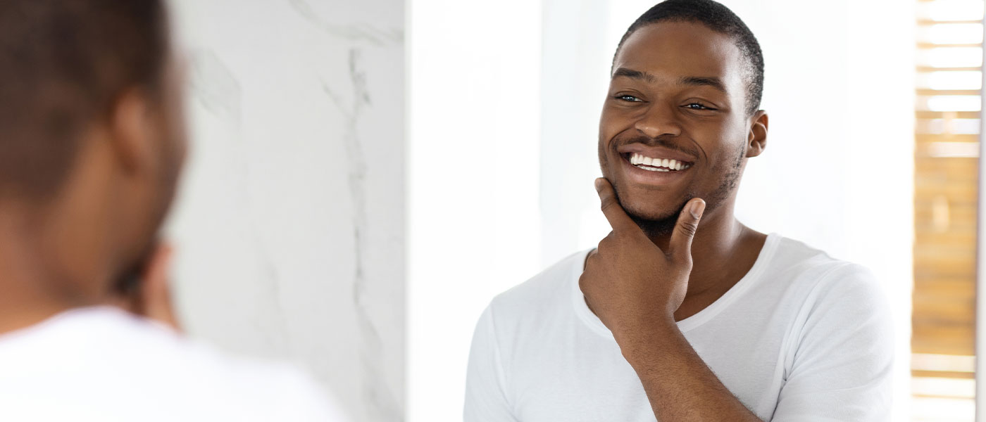Happy man looking in the mirror after a skin treatment from Genesis Lifestyle Medicine.