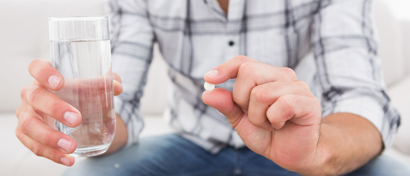 Man holding finasteride and a cup of water at Genesis Lifestyle Medicine.
