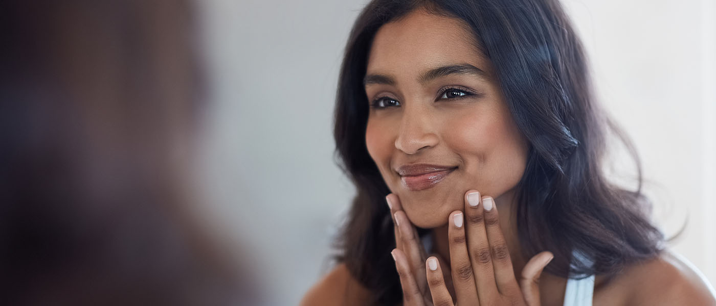 Woman looking in the mirror happy with her skin after treatment from Genesis Lifestyle Medicine.