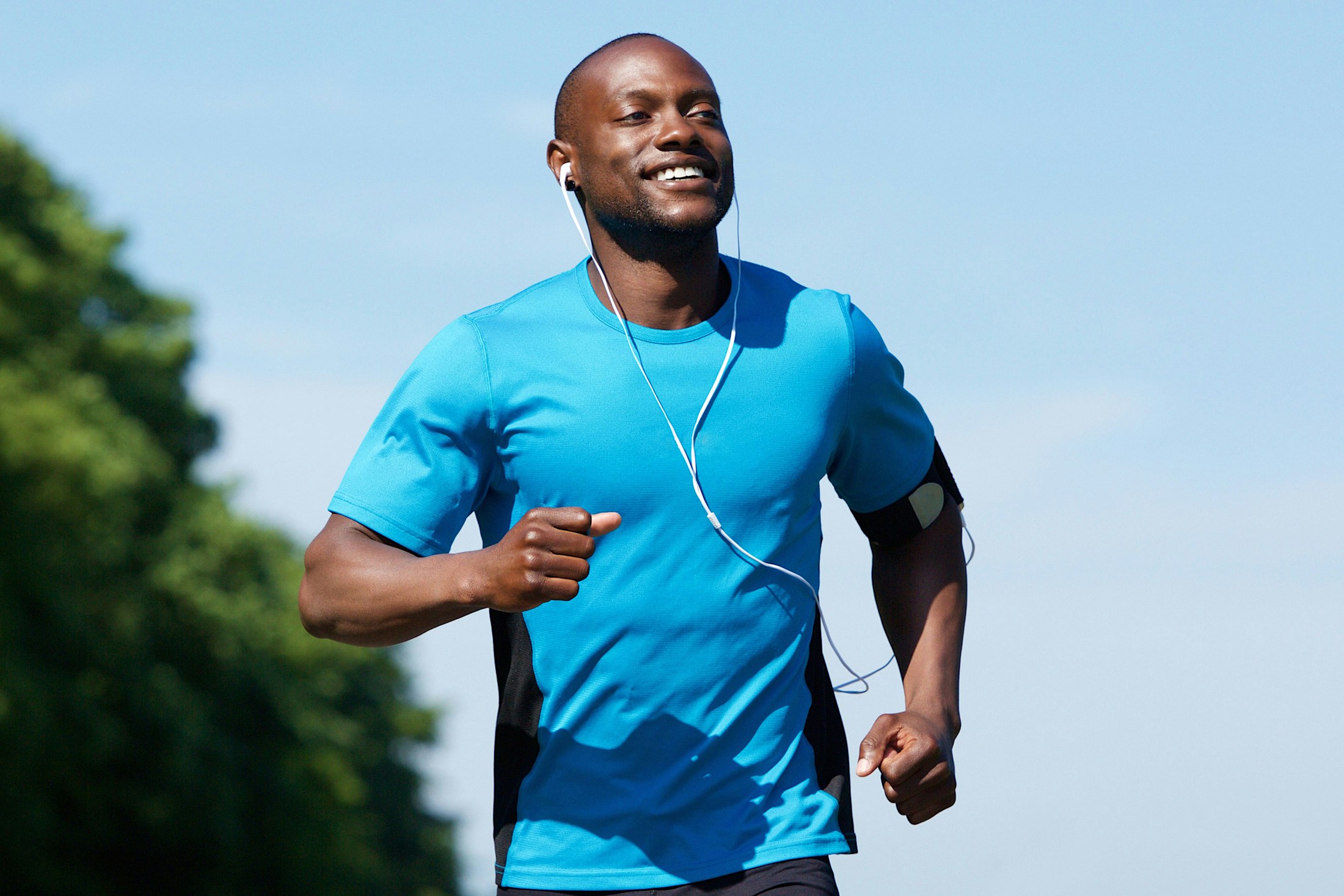 A smiling man running outdoors with headphones in his ears after getting medical weight loss in Denver.