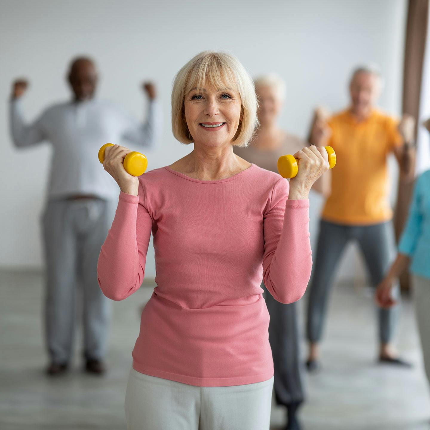an older woman standing in a workout class while holding small dumbells and smiling after getting GLP-1 weight loss medication in Fresno.