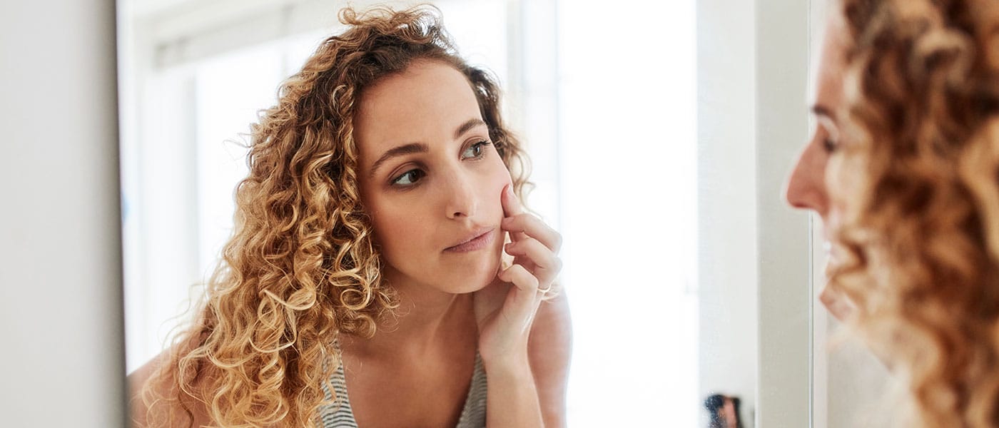 woman looking at her skin in the mirror after starting hormone therapy