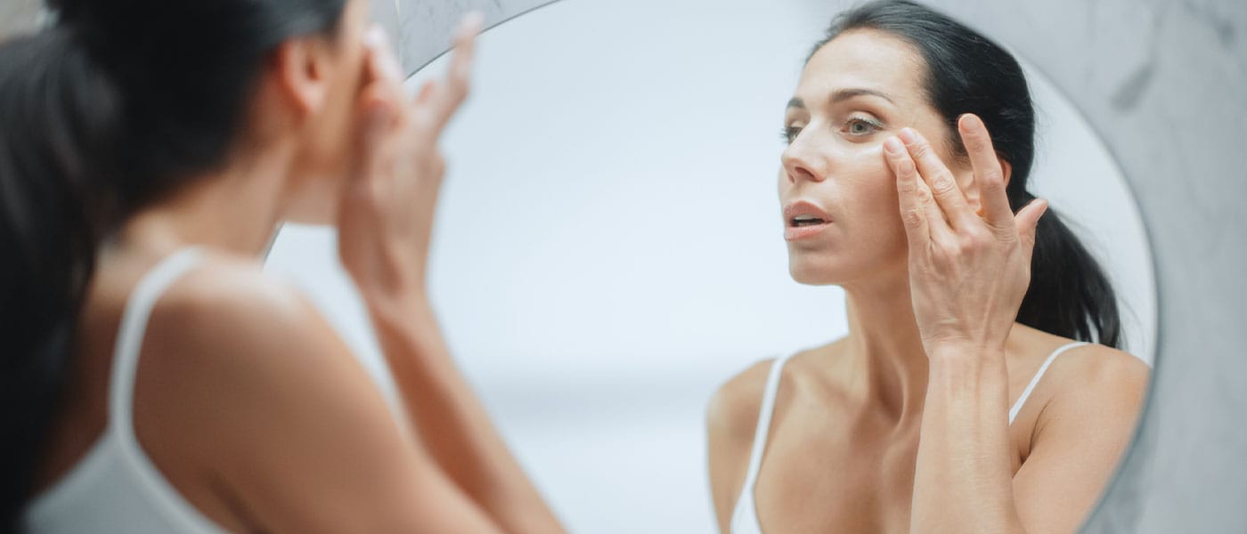 woman looking at her skin in the mirror after starting sermorelin therapy