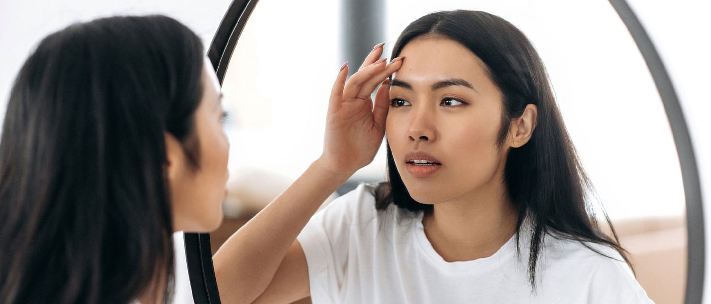 woman looking at her skin in the mirror after a chemical peel