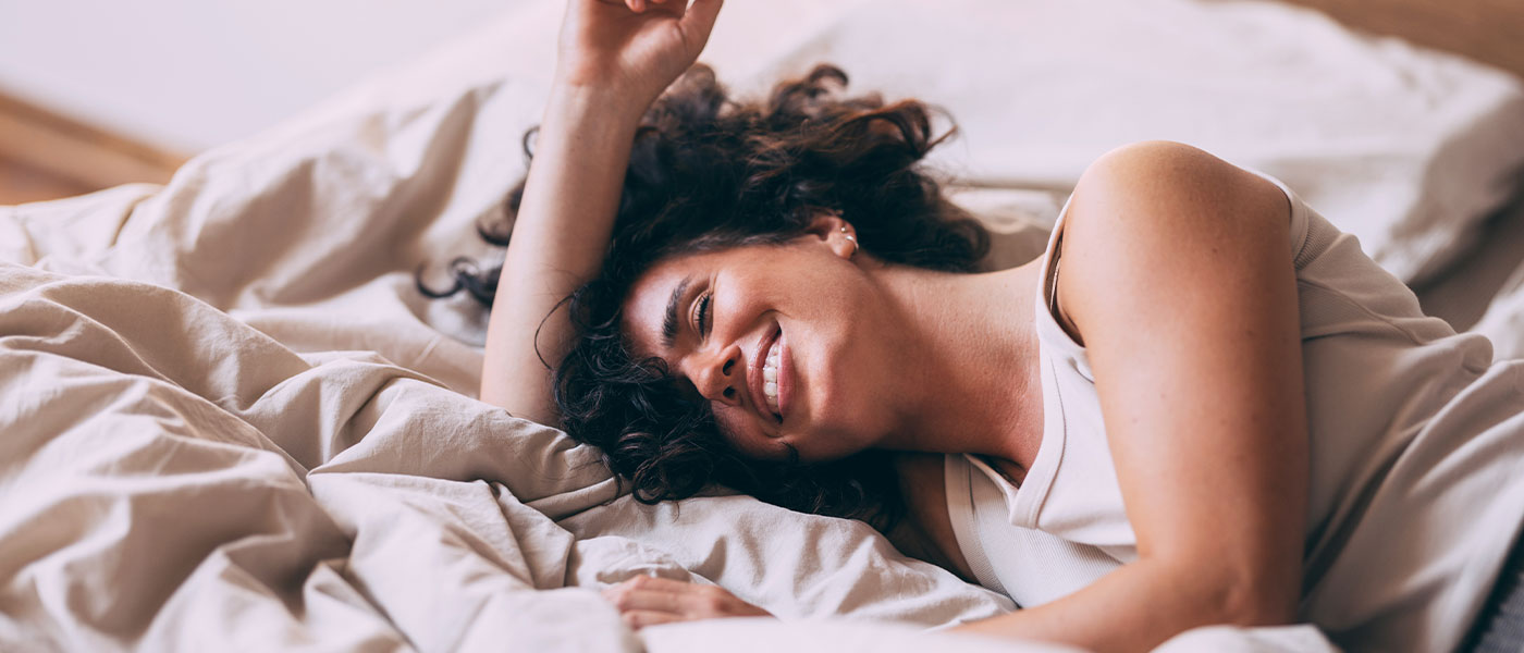 woman in bed smiling after getting the O-Shot