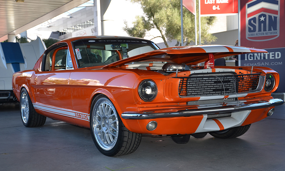 1965 Mustang Fastback featuring Universal Pro Series Low Back seat in SPORT-XR design with beige vinyl, beige suede, white contrast stitching, and silver grommets. Includes matching dash pad, center console, rear seat, headliner, and door panels.