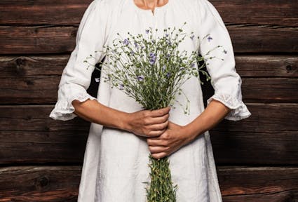 Frau in weissem Leinenkleid hält einen Strauss blau blühender Leinpflanzen